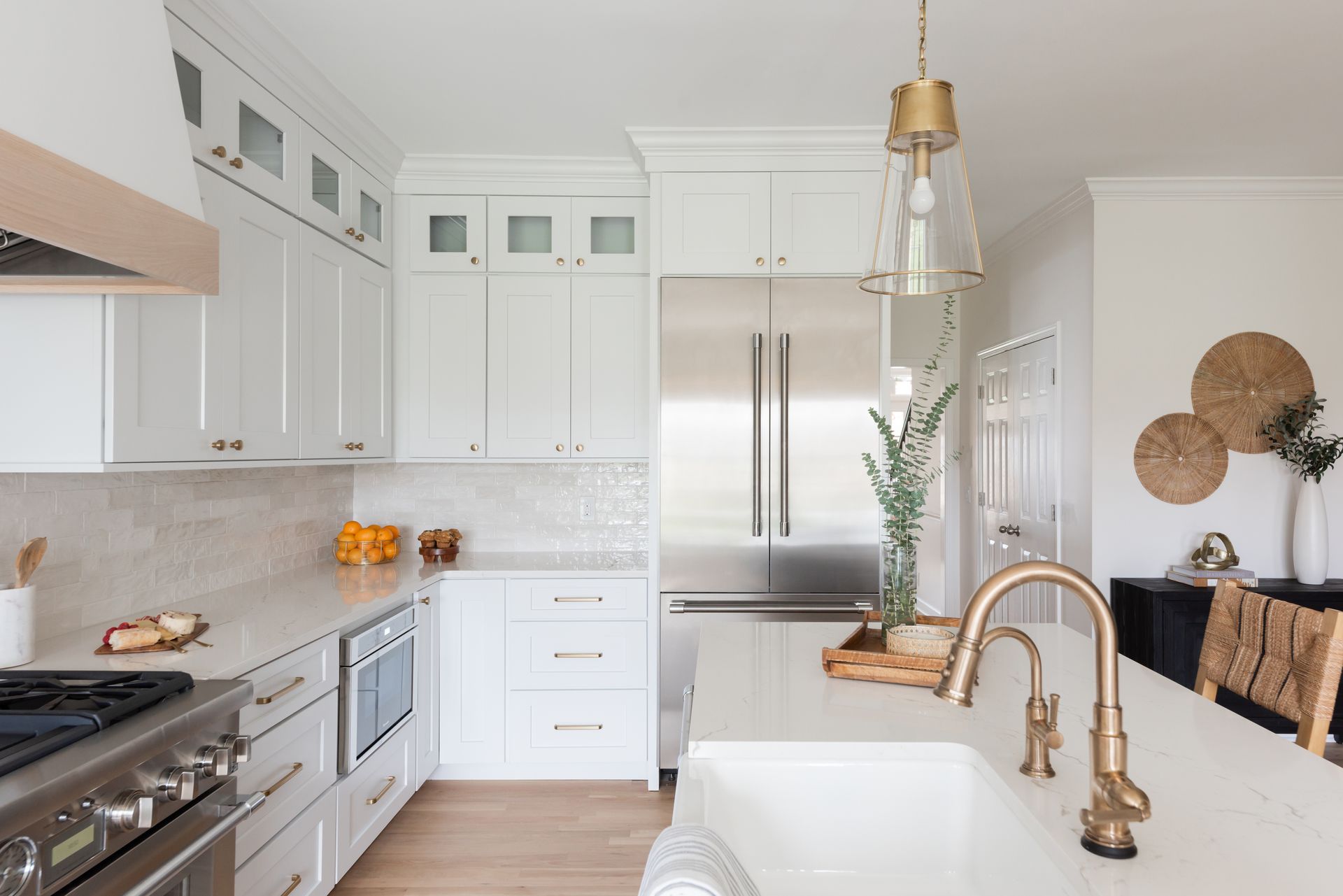 White kitchen with stainless steel appliances, marble countertops, gold faucet, and a pendant light.
