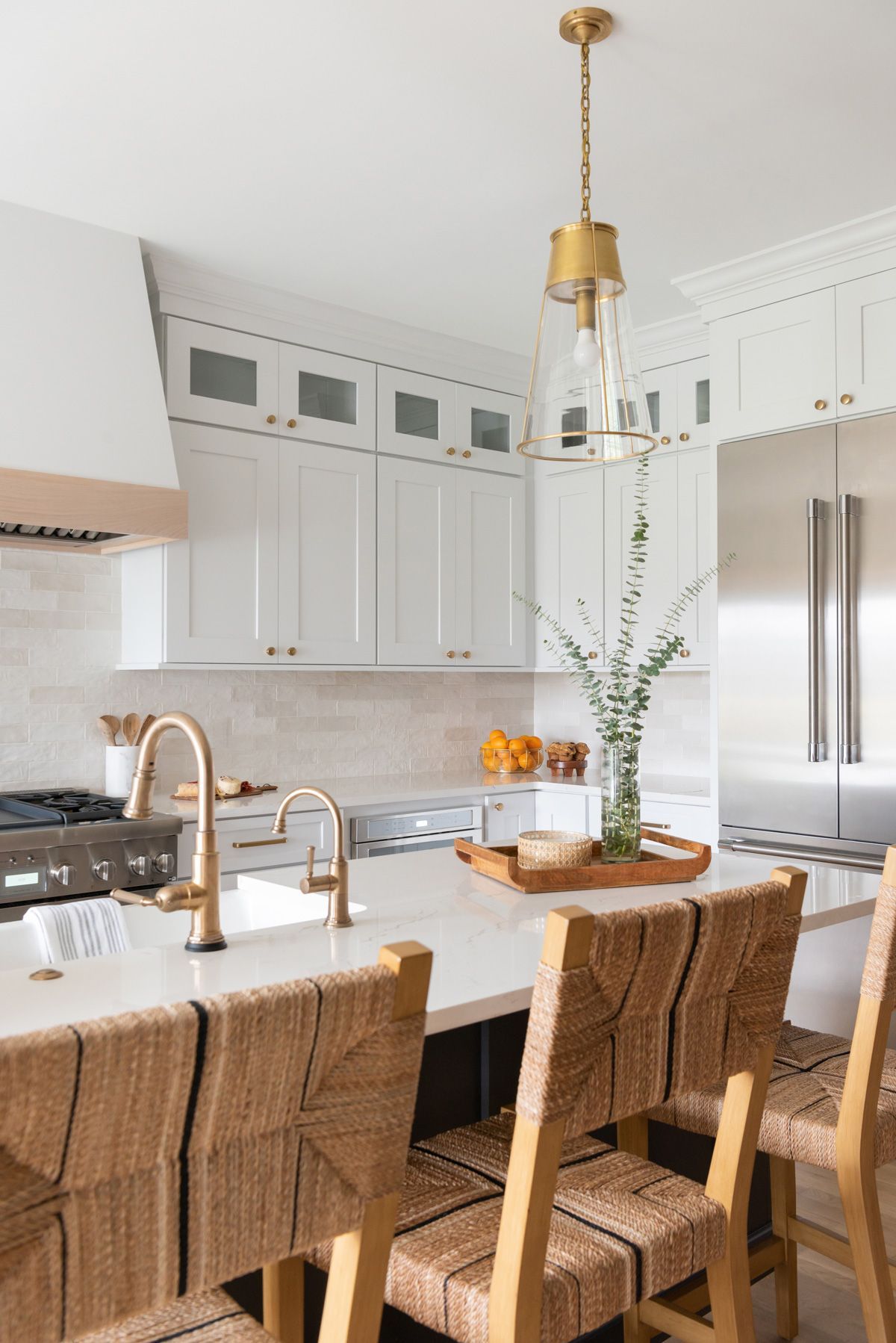 White kitchen with island, rattan bar stools, gold accents, and a pendant light.