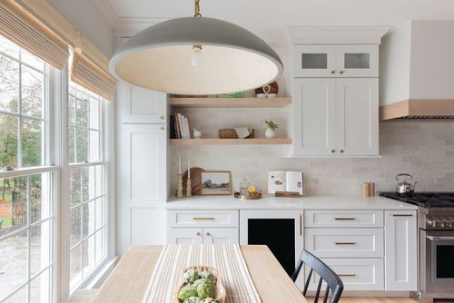 Kitchen with white cabinets, light wood shelves, and a gray pendant light over a wooden table.