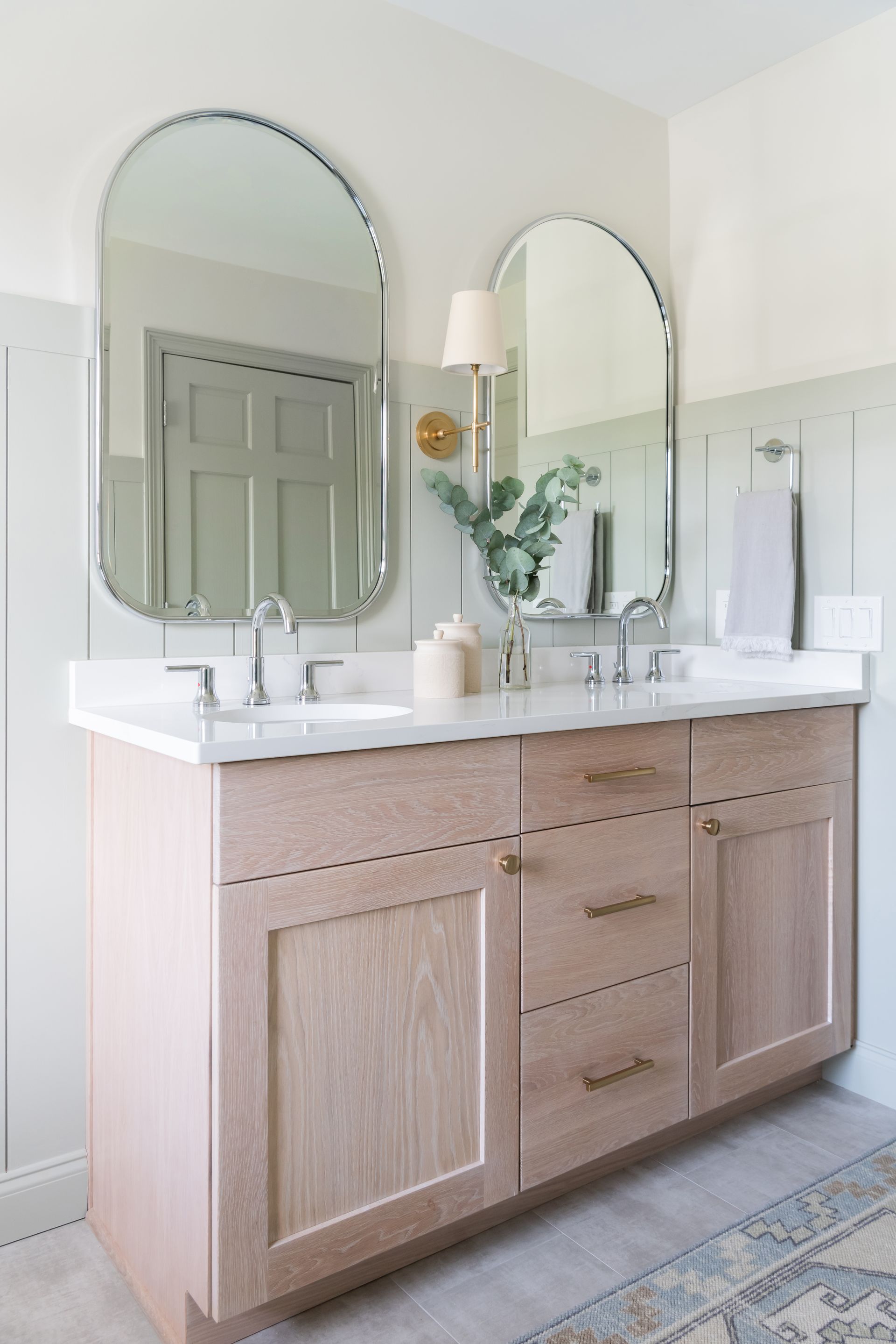 Beige bathroom vanity with marble top, arch mirrors, and gold fixtures.