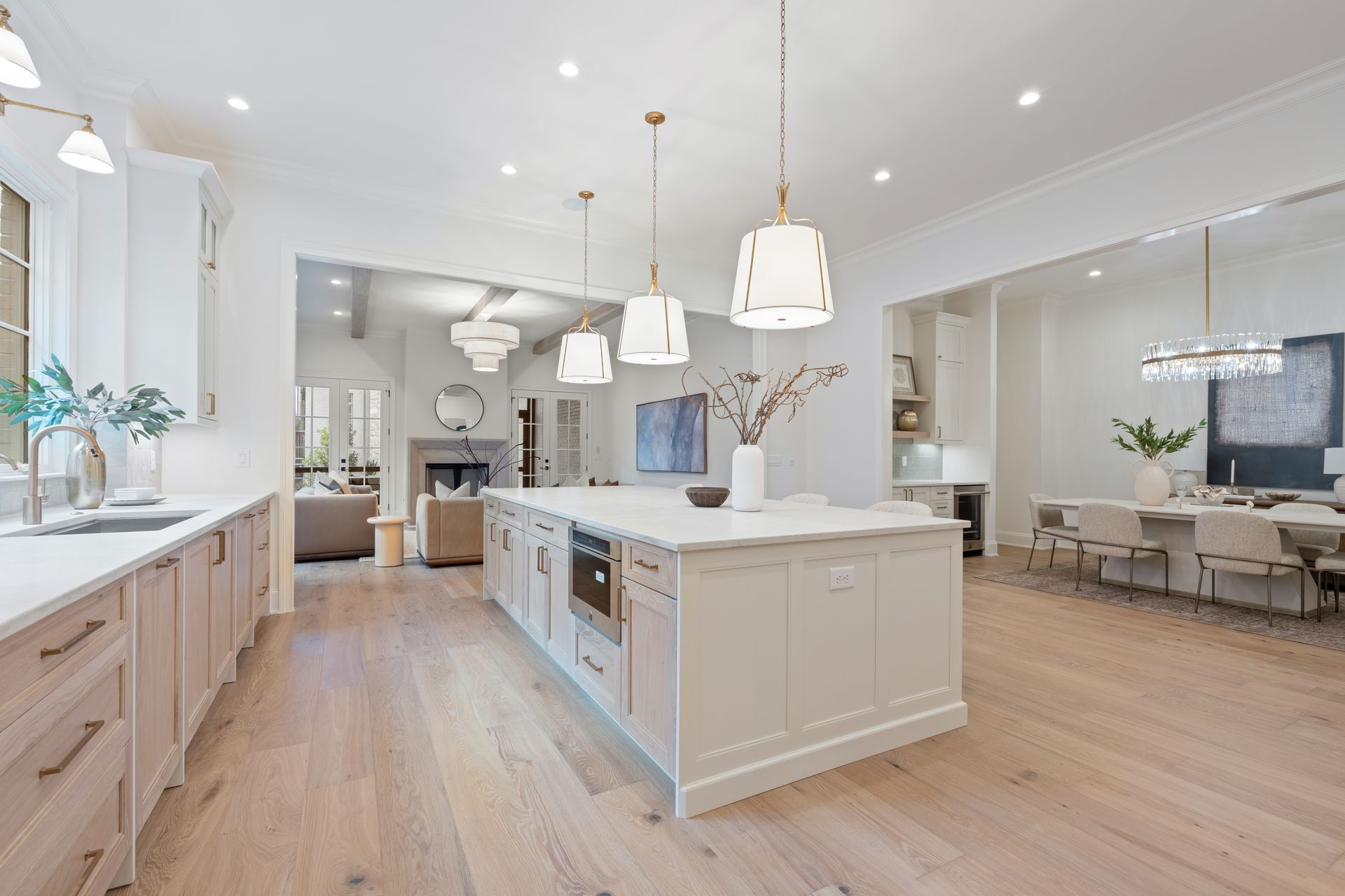 Spacious white kitchen with light wood floors, an island with pendant lights, and an open layout to the dining and living areas.