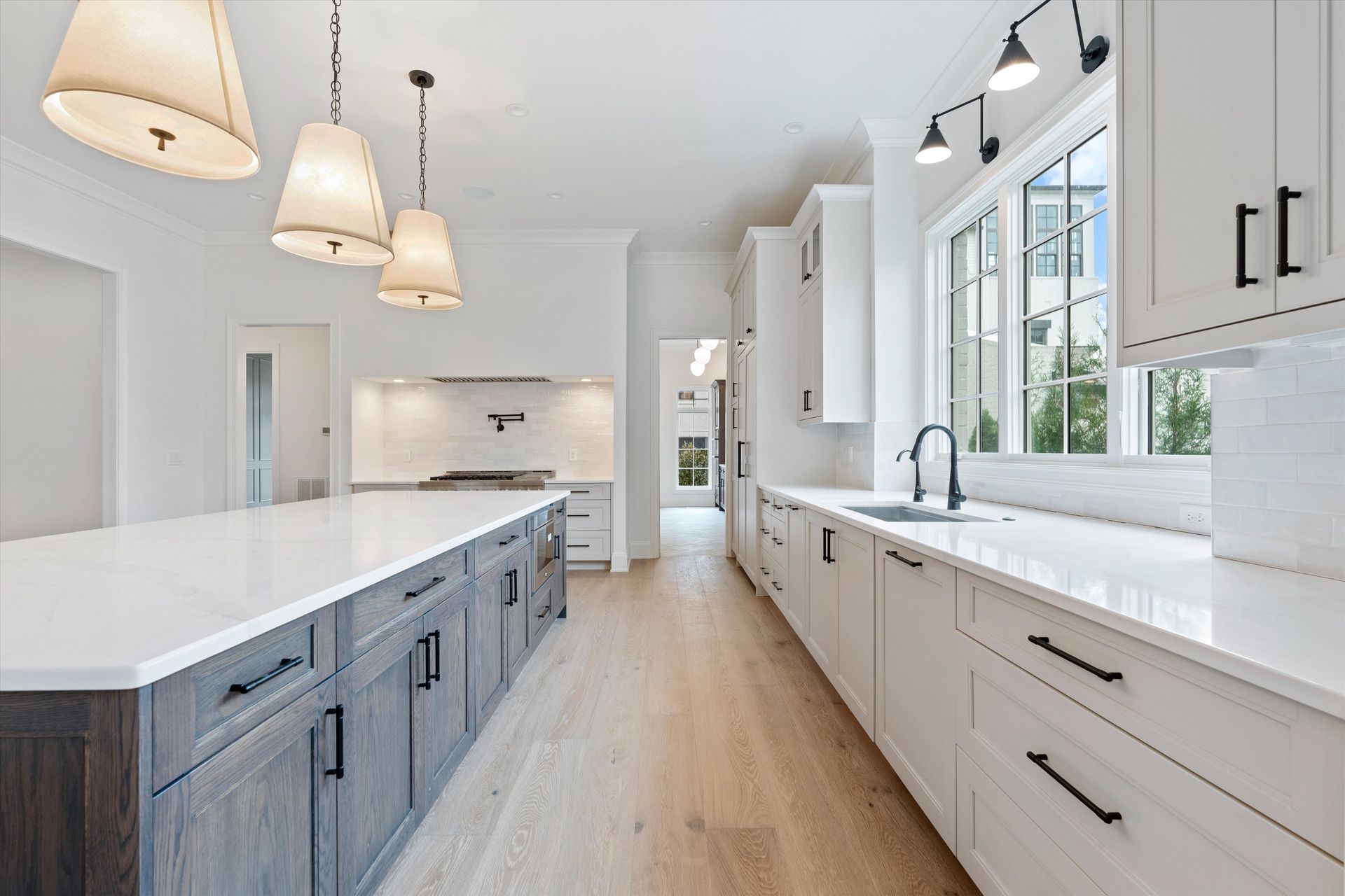 Modern white kitchen with island and light wood flooring.