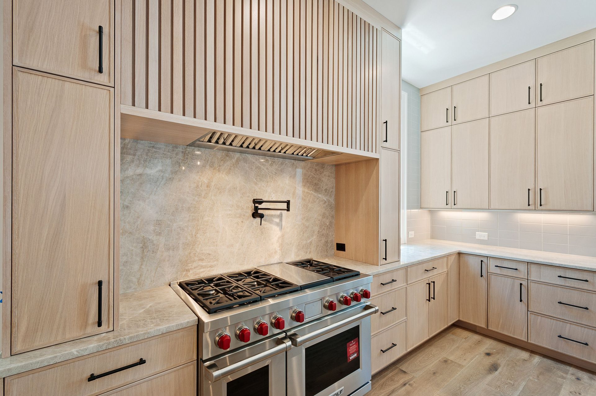 Modern kitchen with light wood cabinetry, stainless steel stove, and marble backsplash.