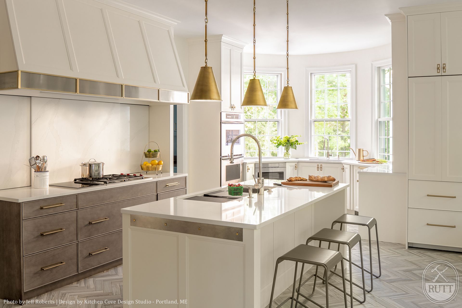 Modern white kitchen with a large island, brass pendant lights, and brown cabinets.
