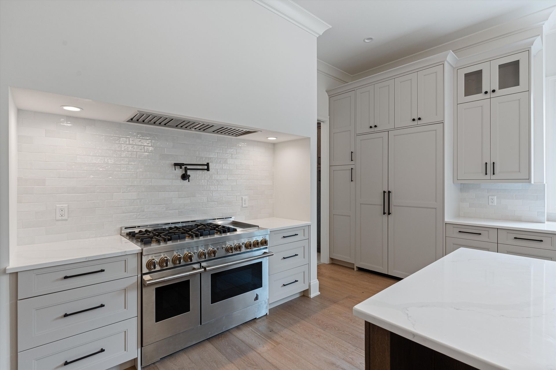 Modern white kitchen with stainless steel oven, white cabinets, and island.