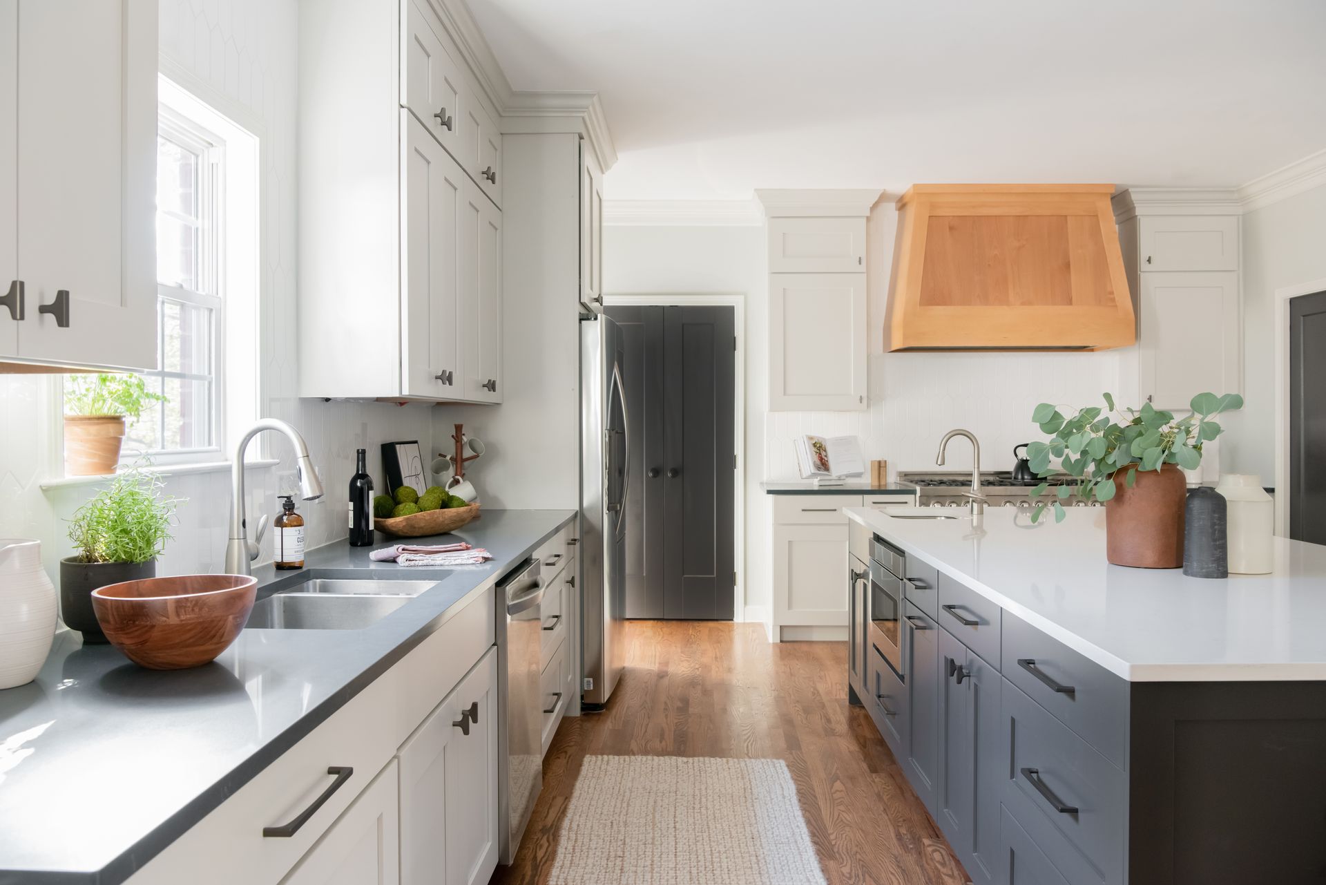 Bright, modern kitchen with white cabinets, dark gray countertops, and a wooden range hood.