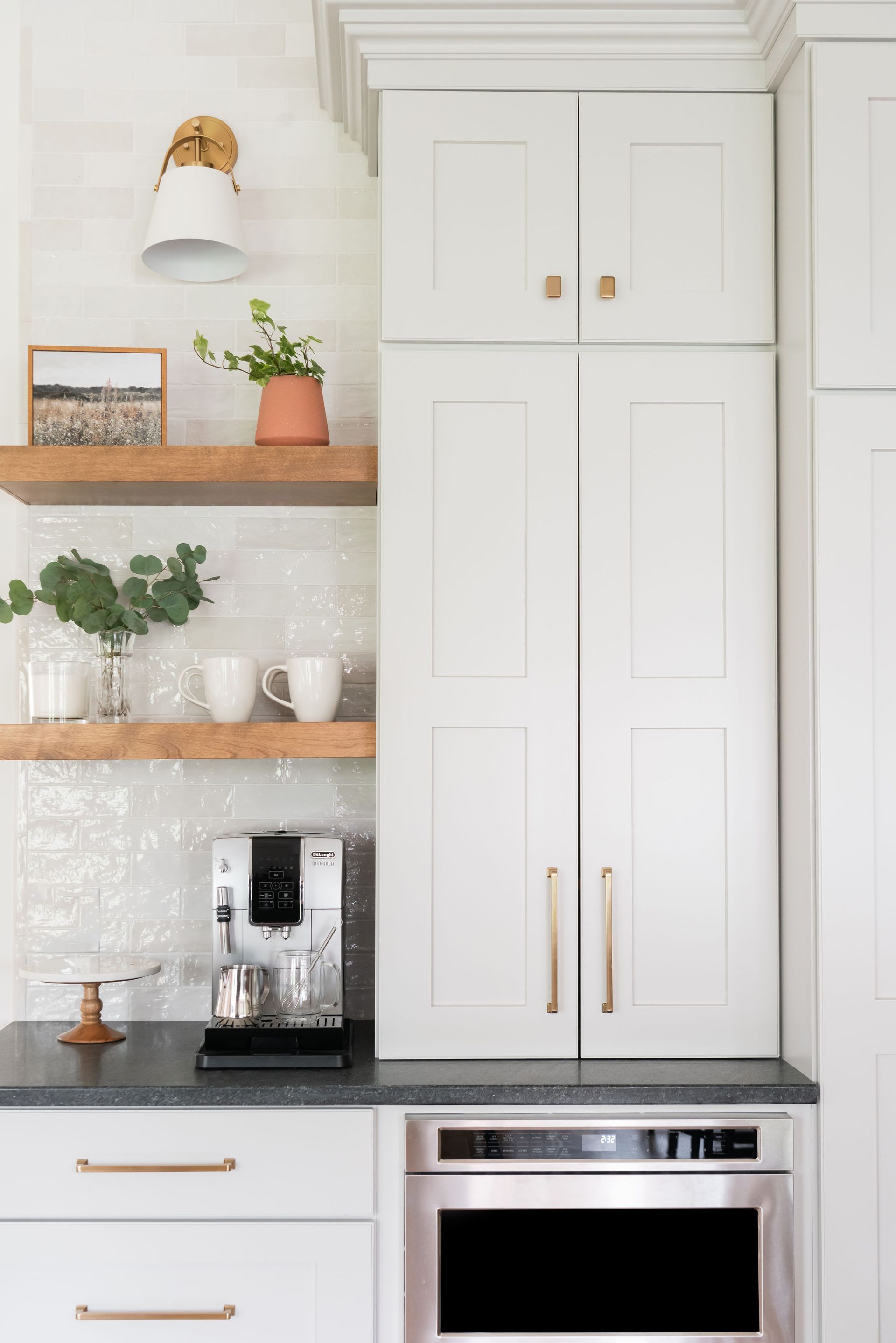 Kitchen corner with white cabinets, built-in microwave, coffee machine, and floating shelves with decor.