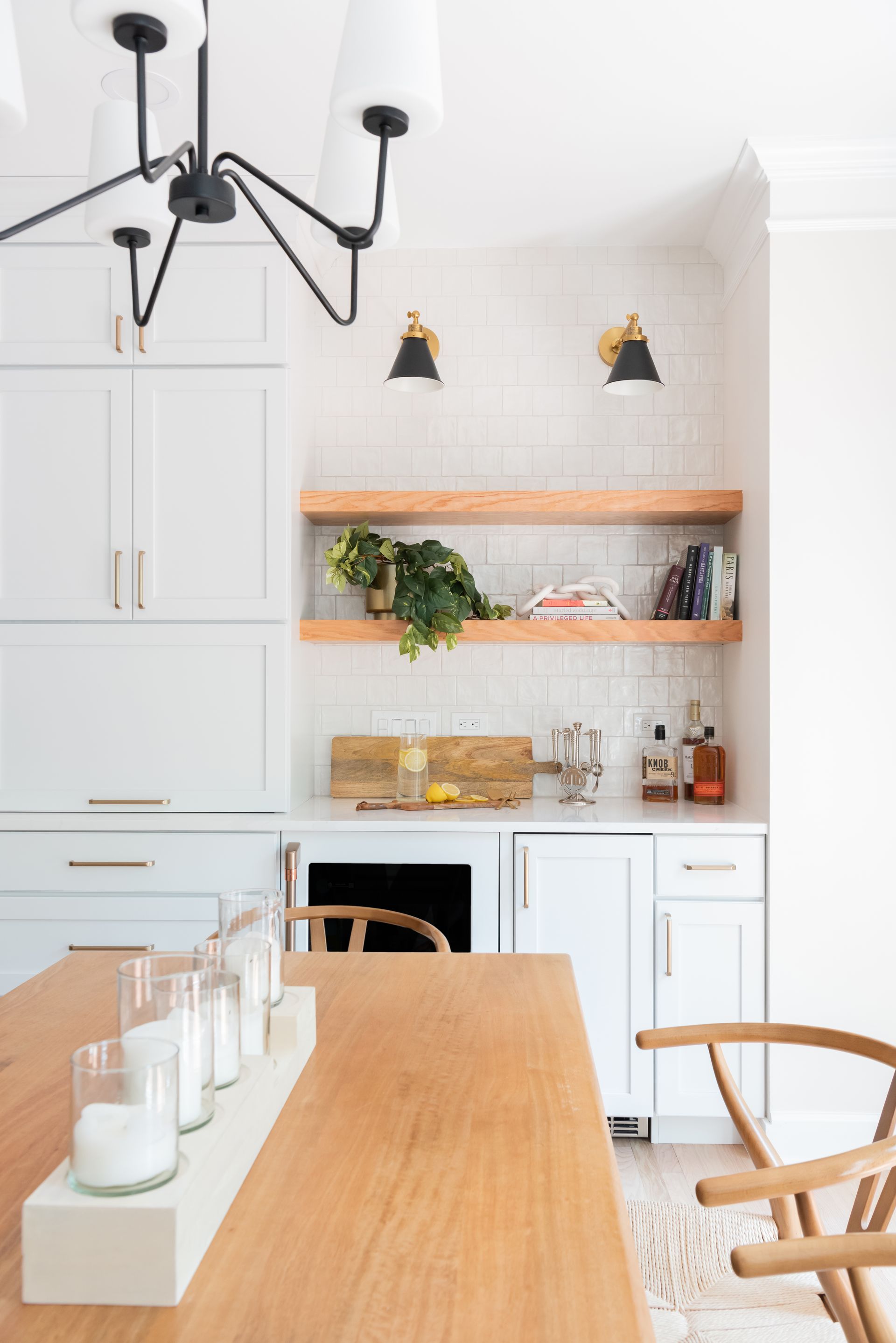 Modern kitchen with light blue cabinetry, wood shelves, black sconces, and a black chandelier.
