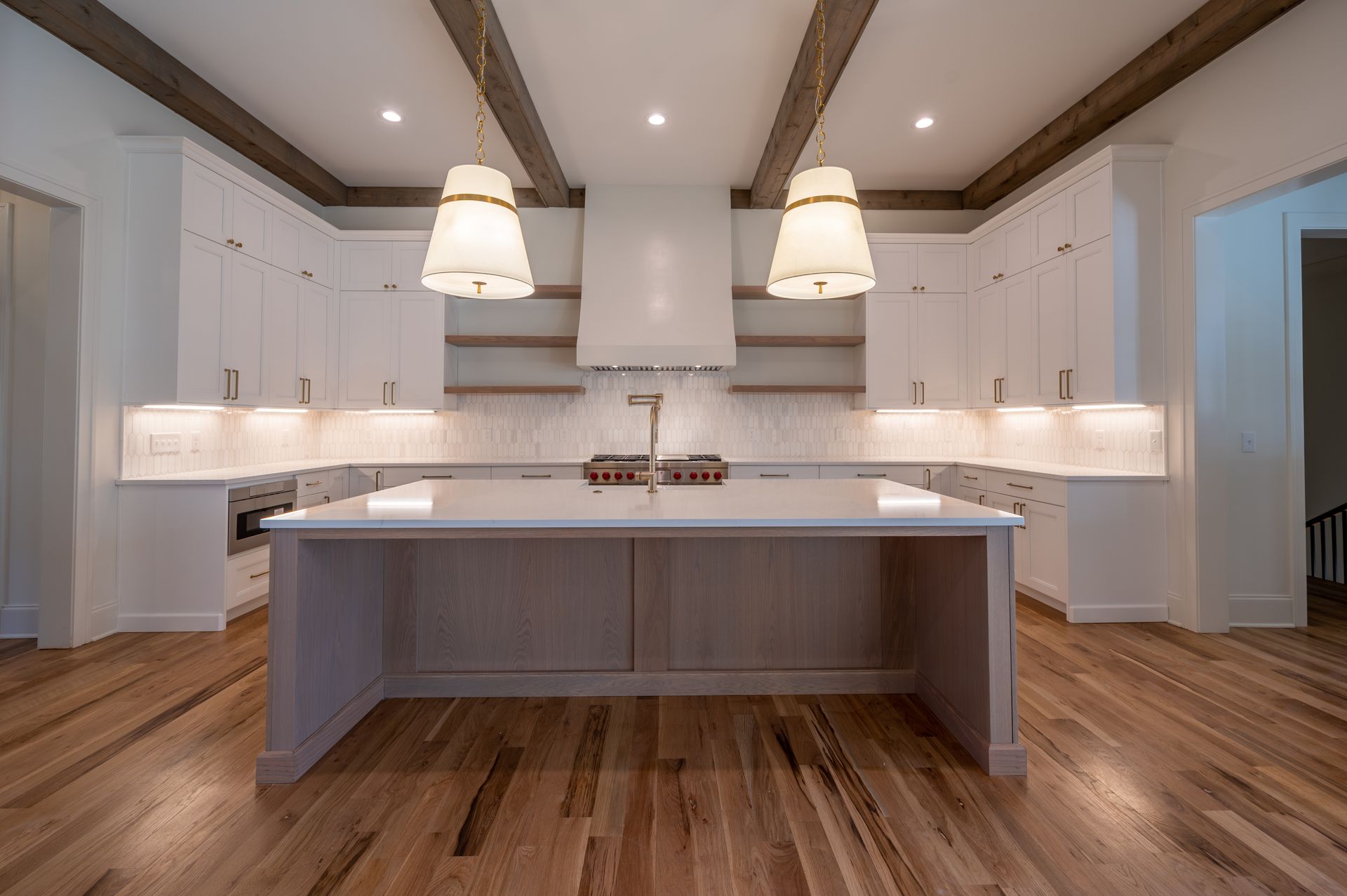 Modern white kitchen with island, wood floor, recessed lighting, and hanging pendant lights.