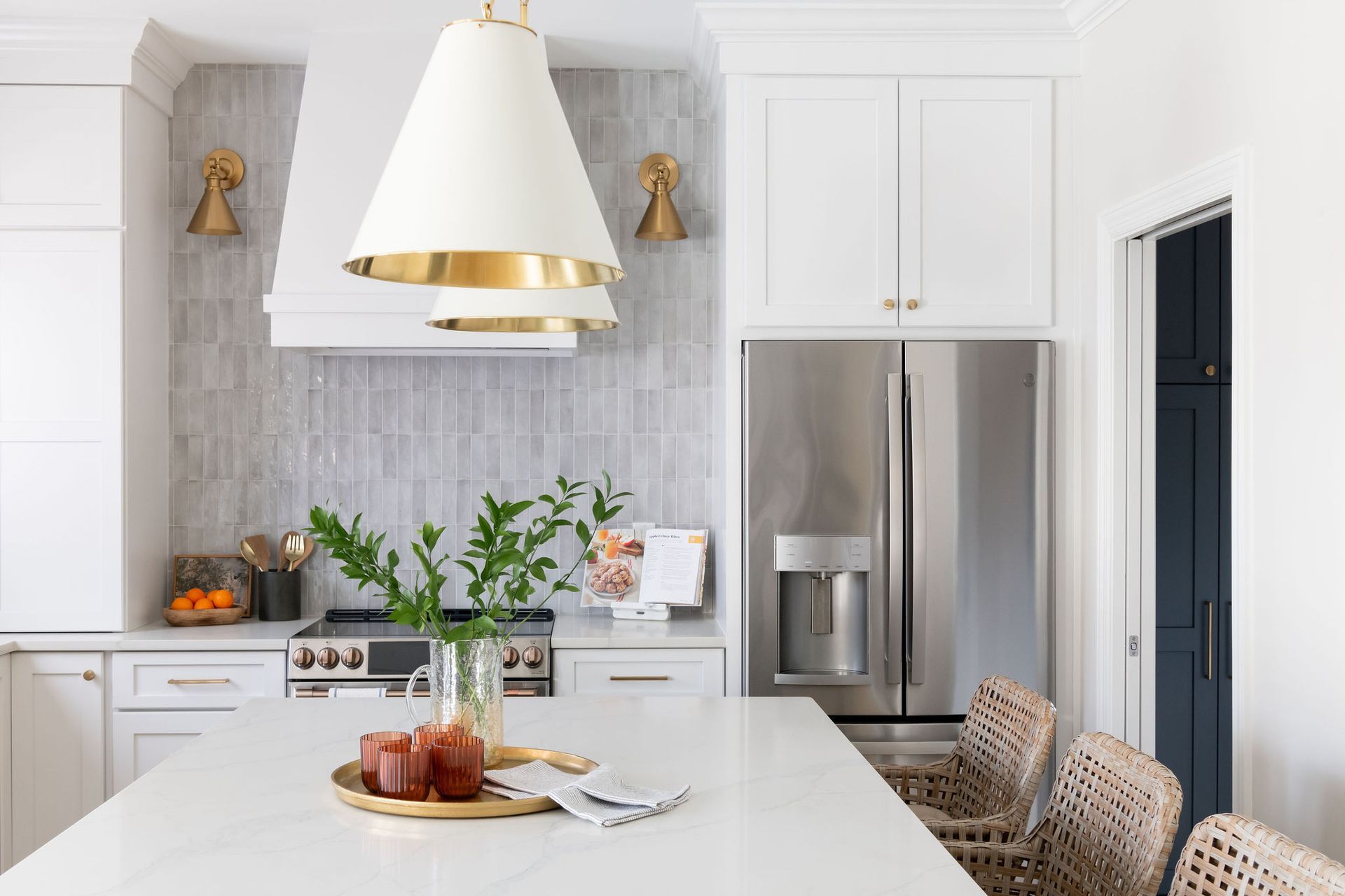 White kitchen with island, stainless steel refrigerator, and gold pendant lights.