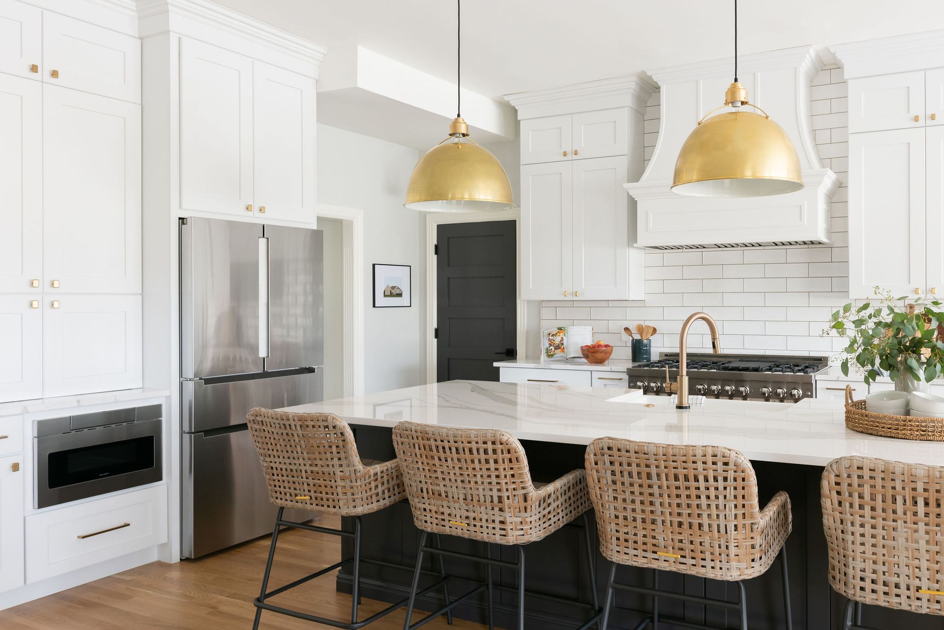 Kitchen with white cabinets, gold pendant lights, and a dark island with woven bar stools.