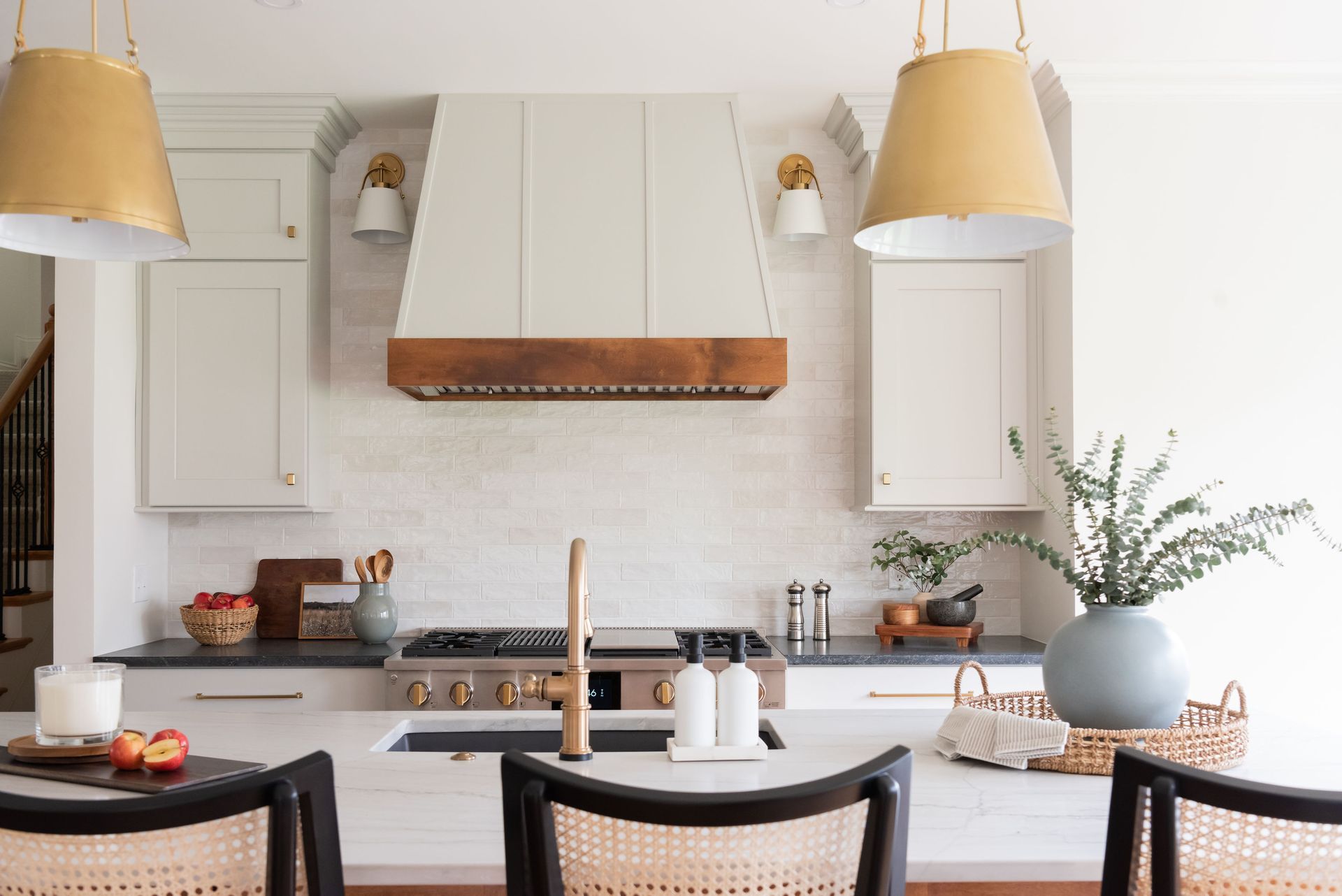 Kitchen with white cabinets, gold pendant lights, and island with woven chairs.