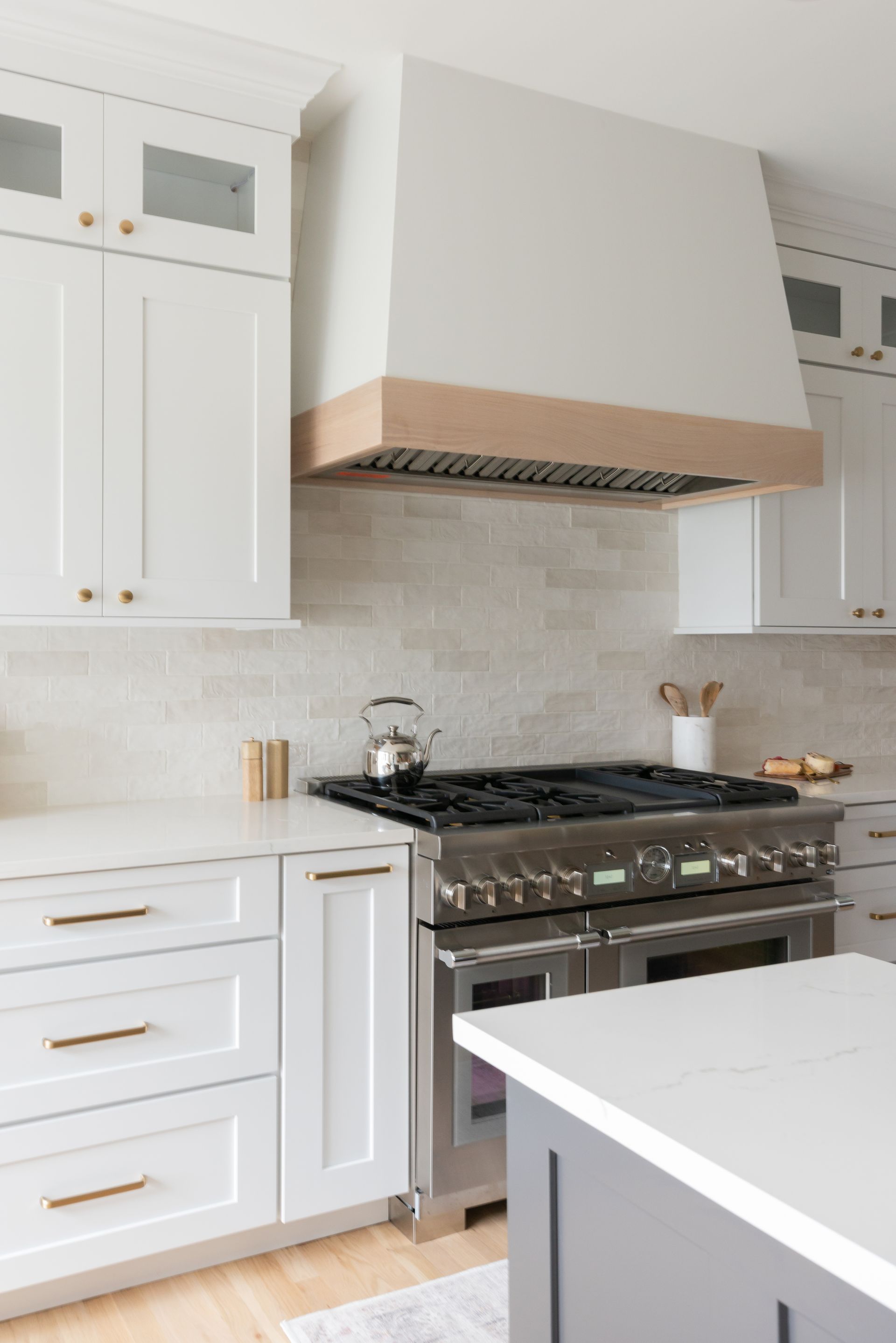 Modern kitchen with white cabinets, stainless steel range, and light wood range hood.