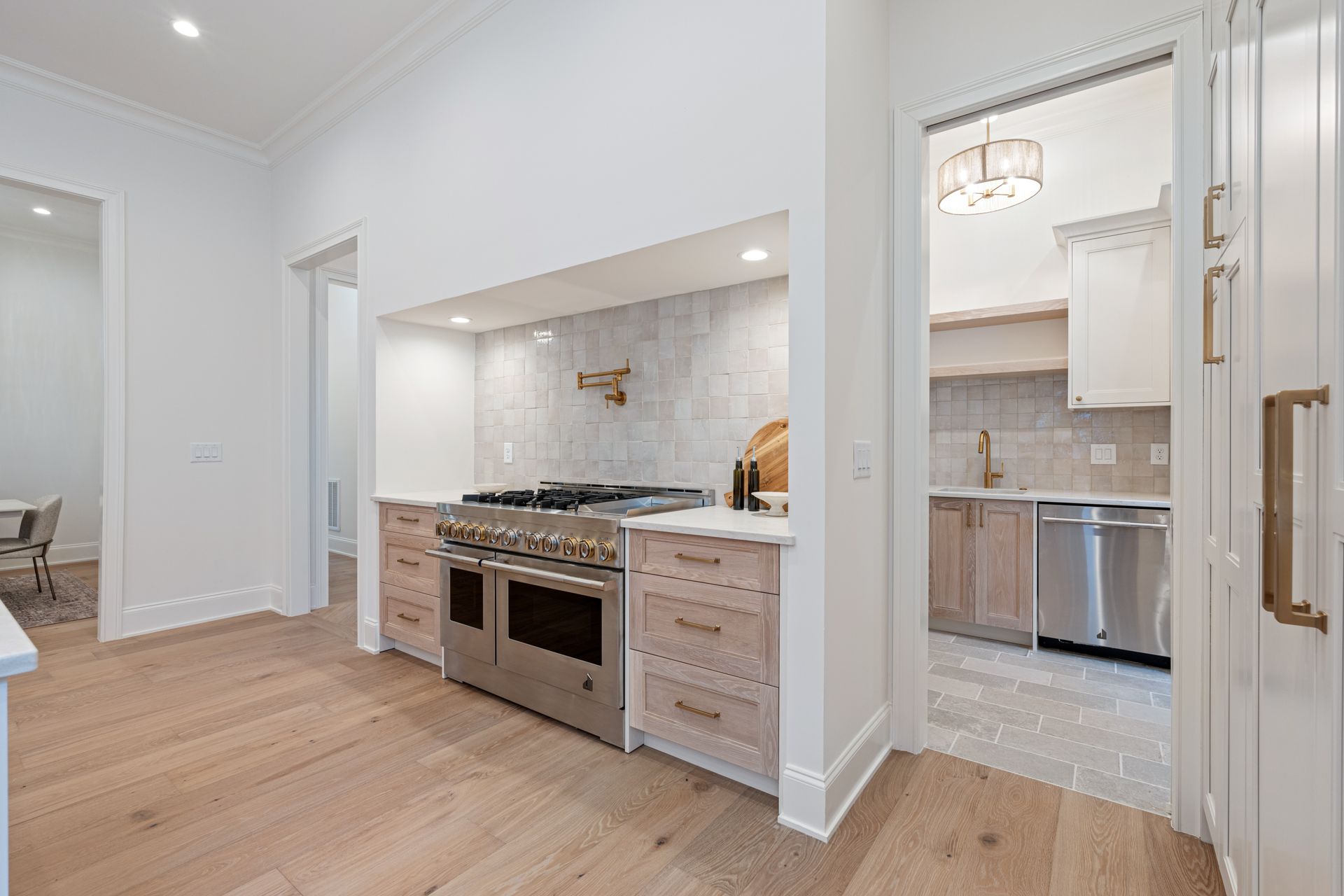 Modern kitchen with a stainless steel range, light wood cabinets, and doorway to another area.