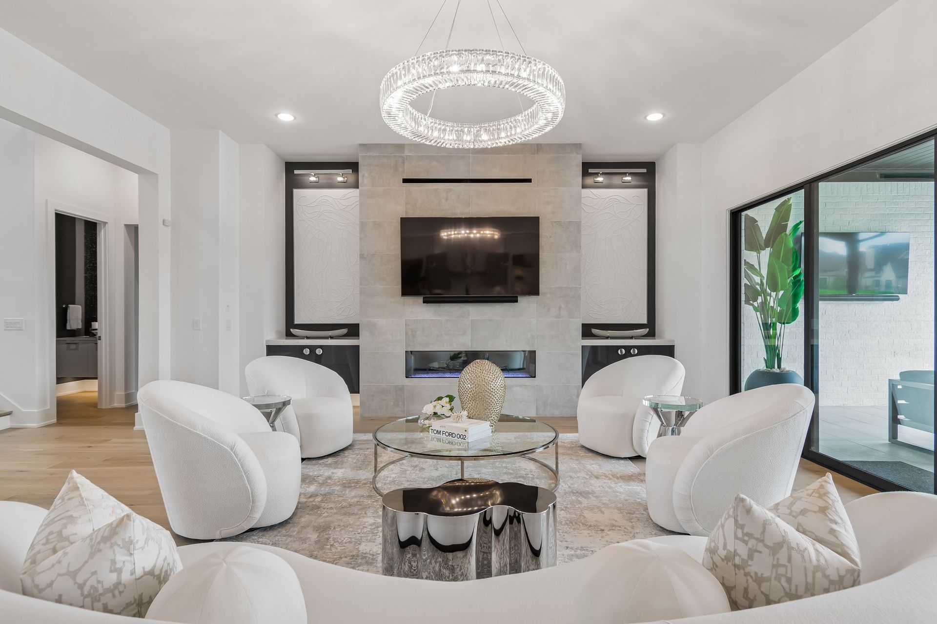 Living room with modern furnishings: white chairs, sectional sofa, fireplace, and chandelier.