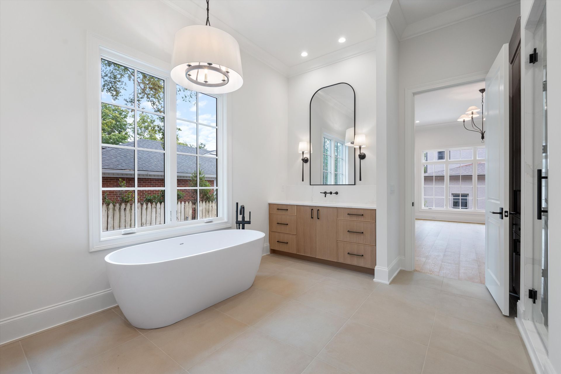 Spacious, modern bathroom with freestanding tub, vanity, large window, and light wood cabinetry.