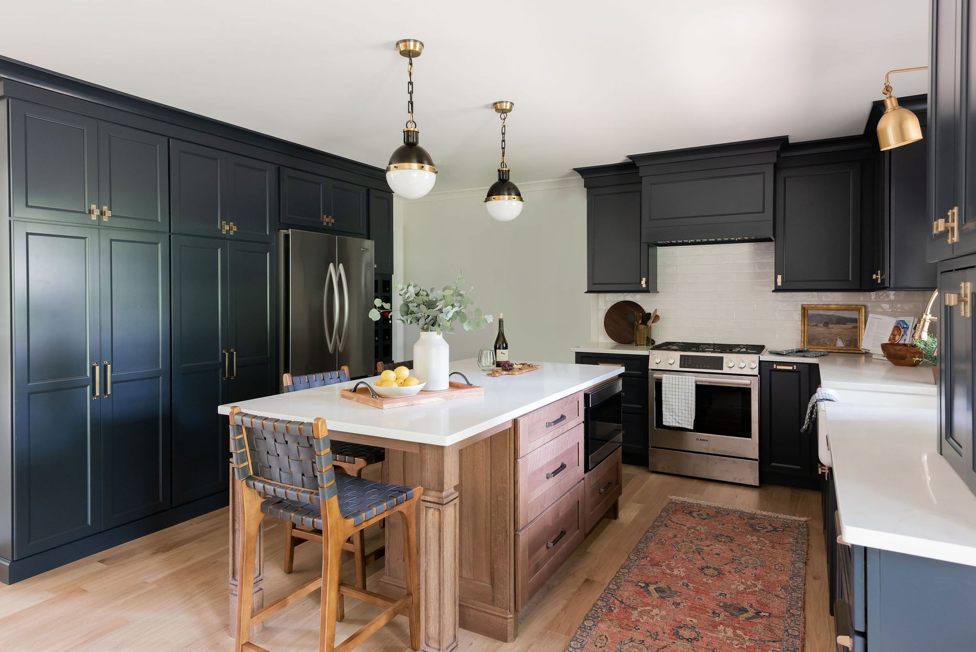 Navy kitchen with light wood floor, white countertops, and wooden island; includes gold hardware, light fixtures, and a rug.