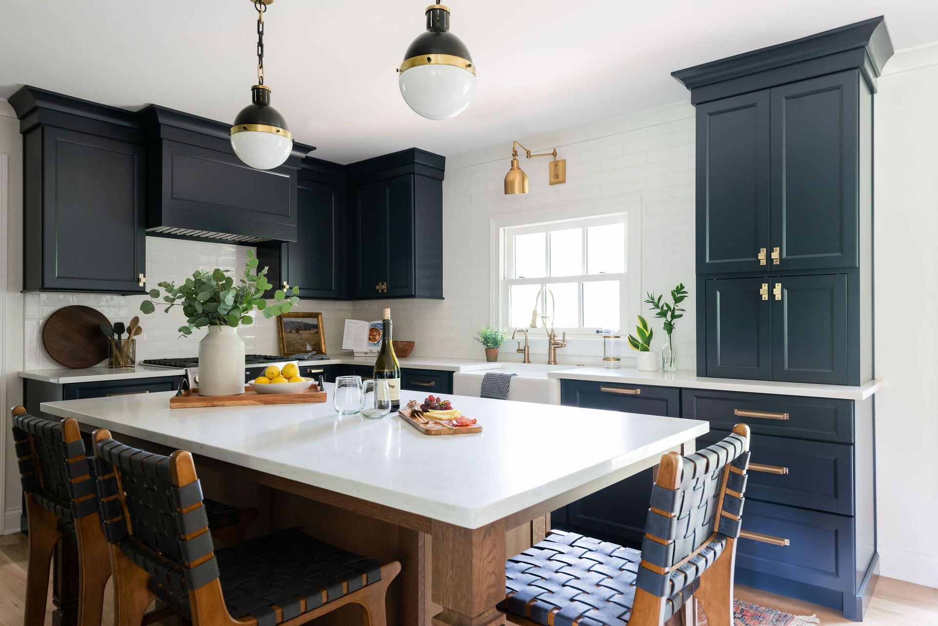 Modern kitchen with dark blue cabinets, white countertops, island with seating, and gold accents.
