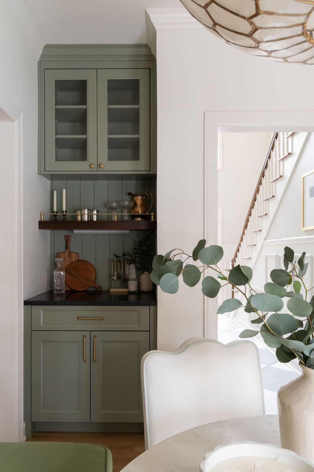 A small green built-in bar area with upper glass cabinets and lower cabinets, with a black countertop.