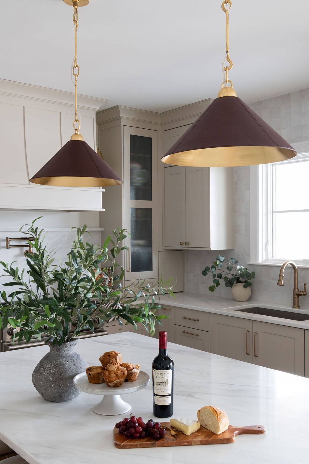 Kitchen with burgundy pendant lights over a marble-topped island with snacks and wine.