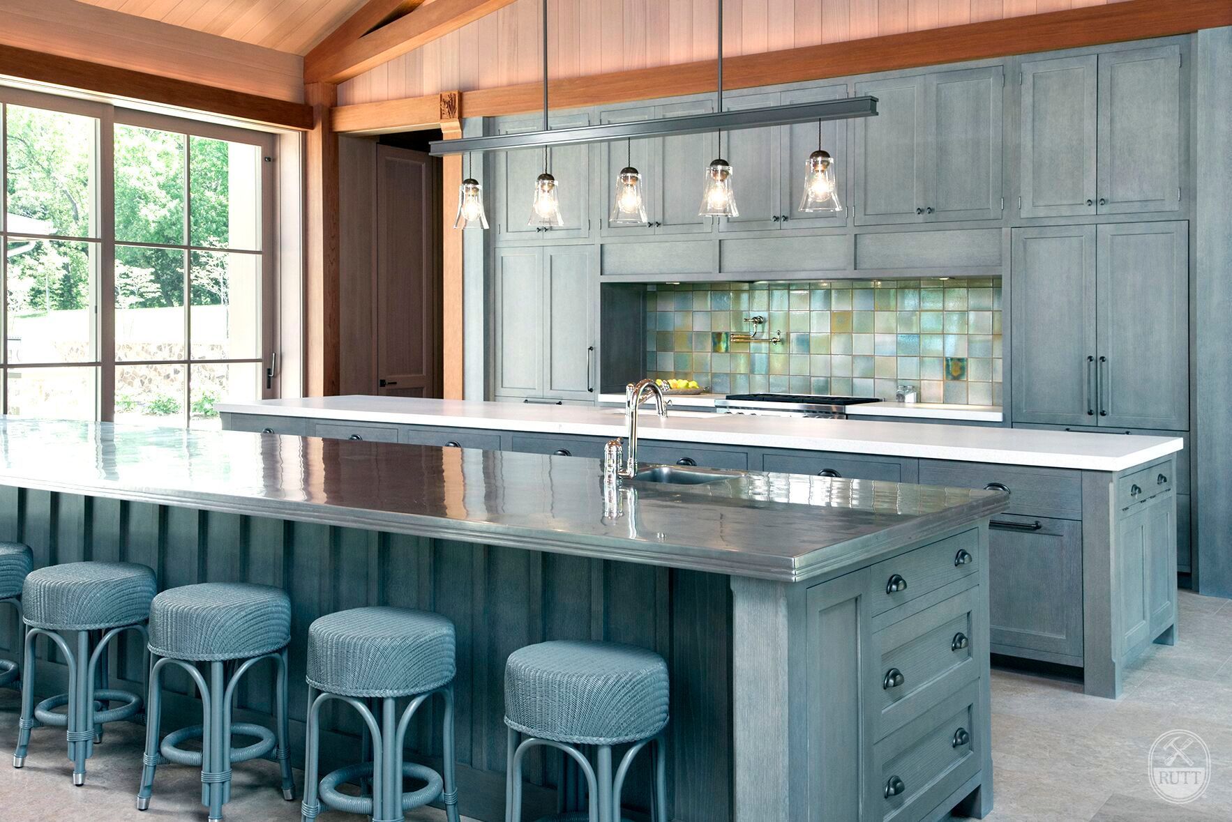 Modern kitchen with two islands, gray cabinets, stools, and pendant lights.