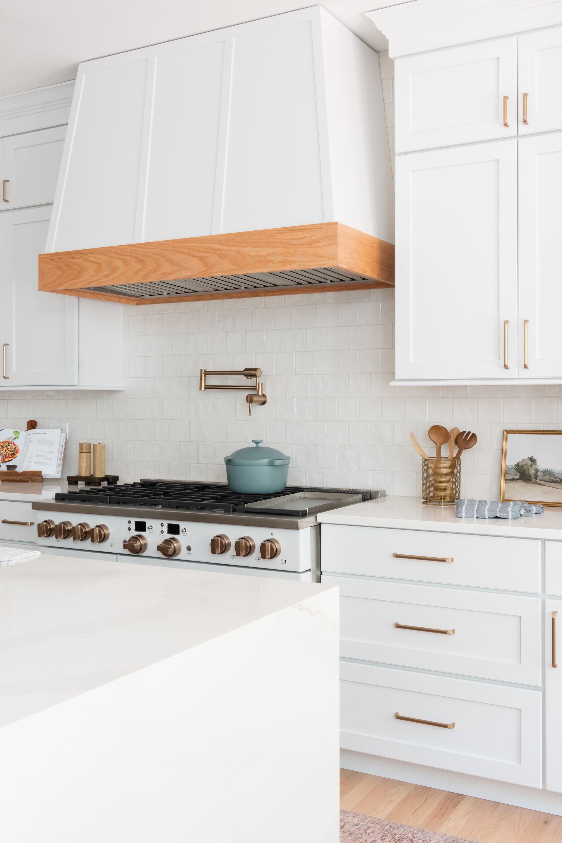 White kitchen with a stove, hood, and cabinetry. The hood has a wood accent.