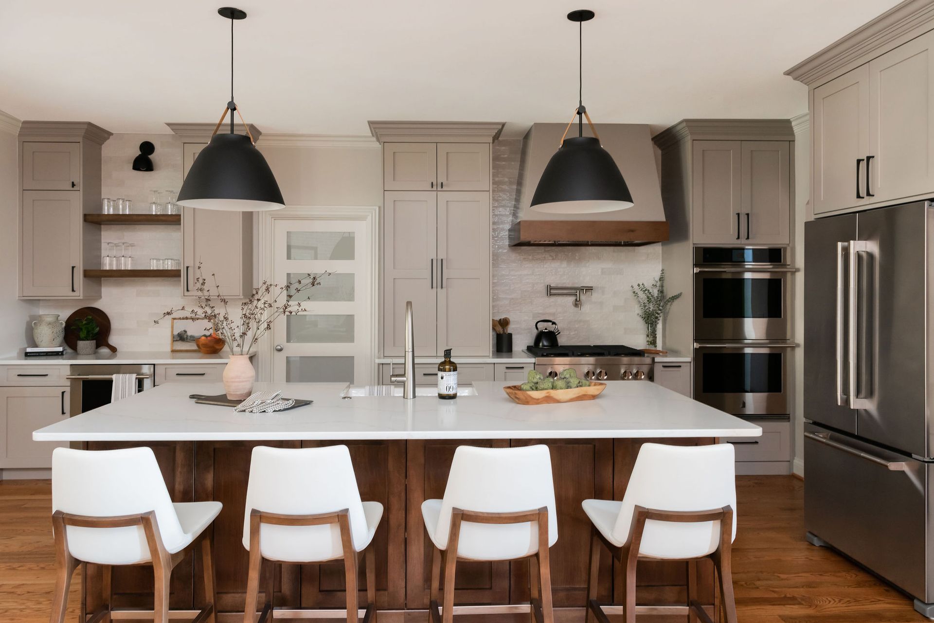 Modern kitchen with gray cabinets, white island with wood accents, and black pendant lights.