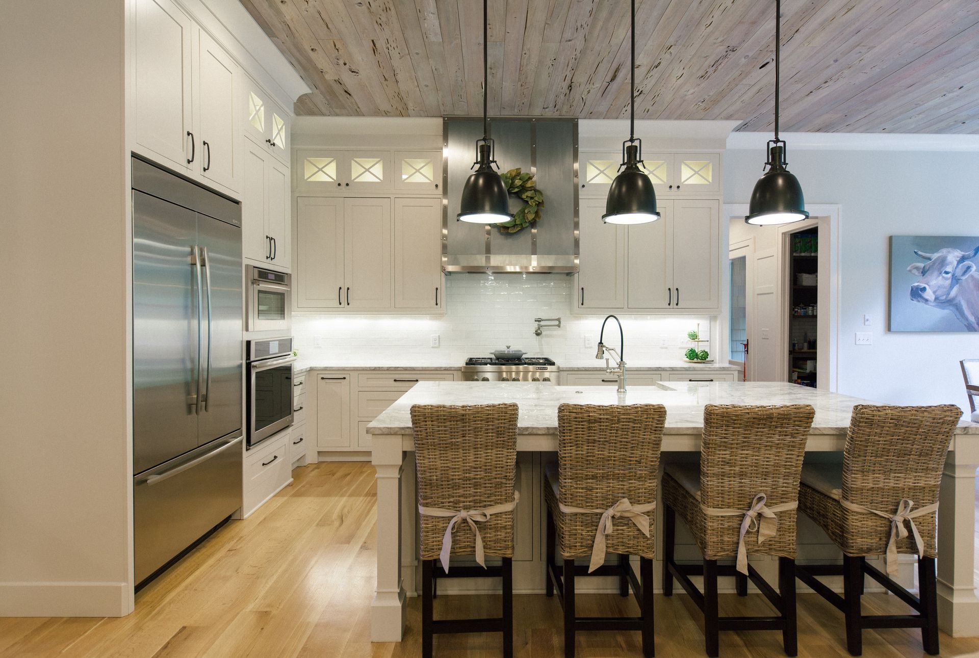 Modern kitchen with white cabinets, stainless steel appliances, island seating, and wood ceiling.