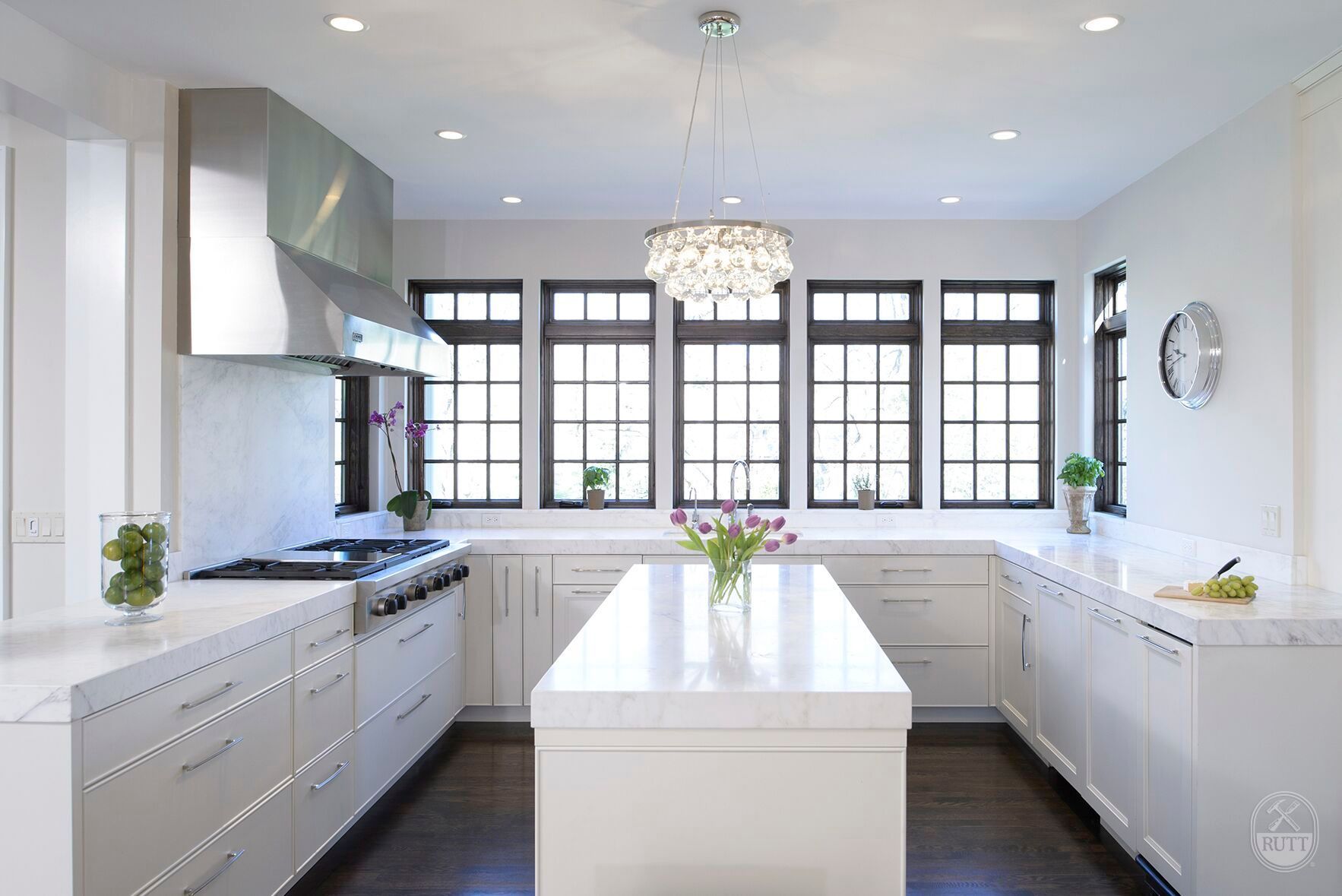 Bright white kitchen with stainless steel appliances, dark framed windows, and a central island.