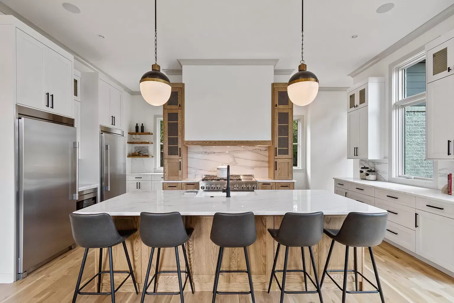 Modern kitchen with white cabinets, large island with seating, stainless steel appliances, and wood accents.