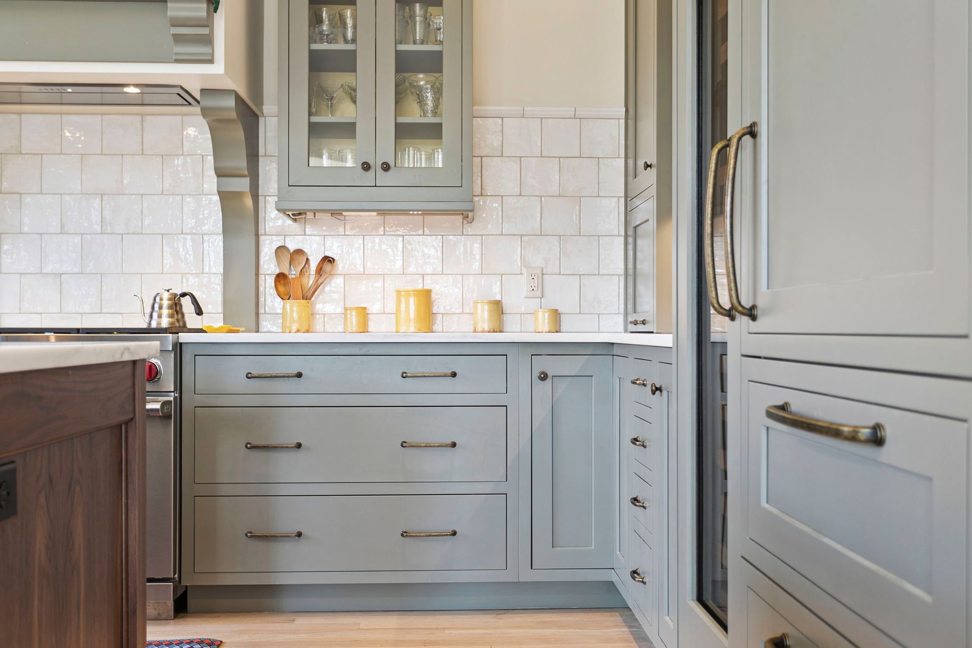 Gray kitchen with white tile backsplash, gray cabinets, light wood floor, and a stainless steel fridge.