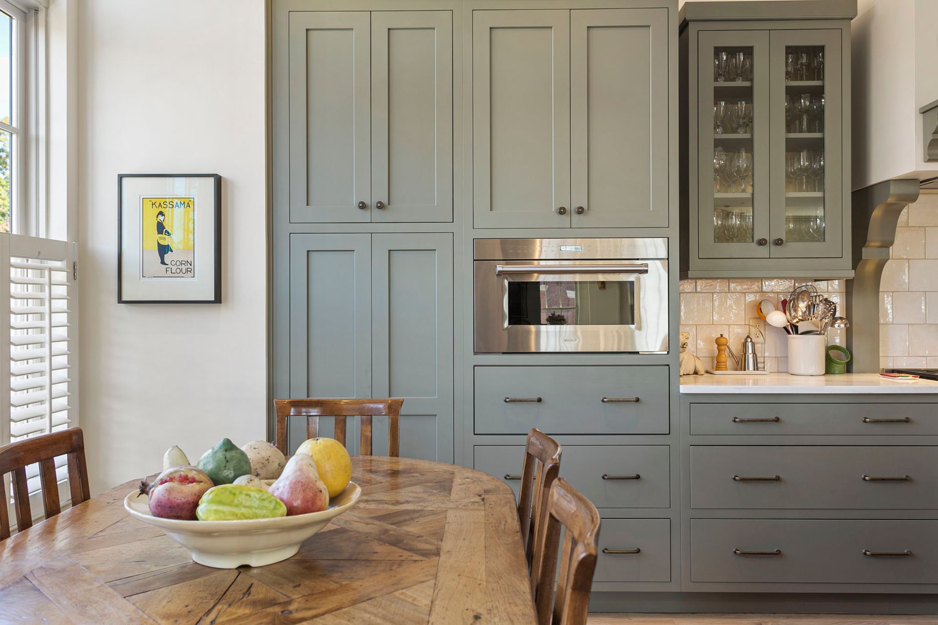 Kitchen with sage green cabinets, built-in microwave, and round wooden table with fruit bowl.