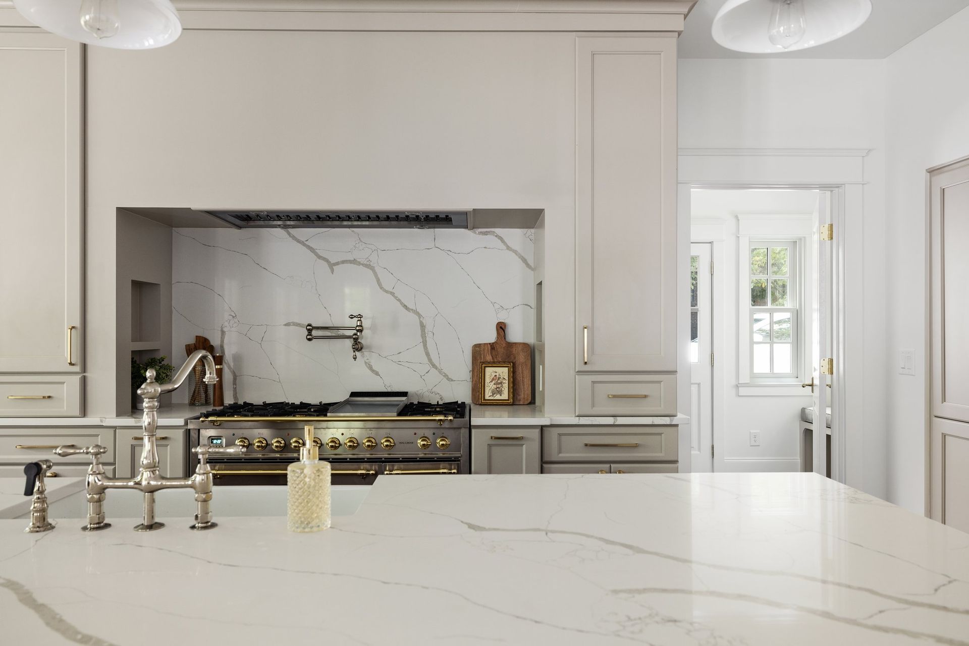 Elegant white kitchen with marble countertops, stainless steel appliances, and a pass-through doorway.
