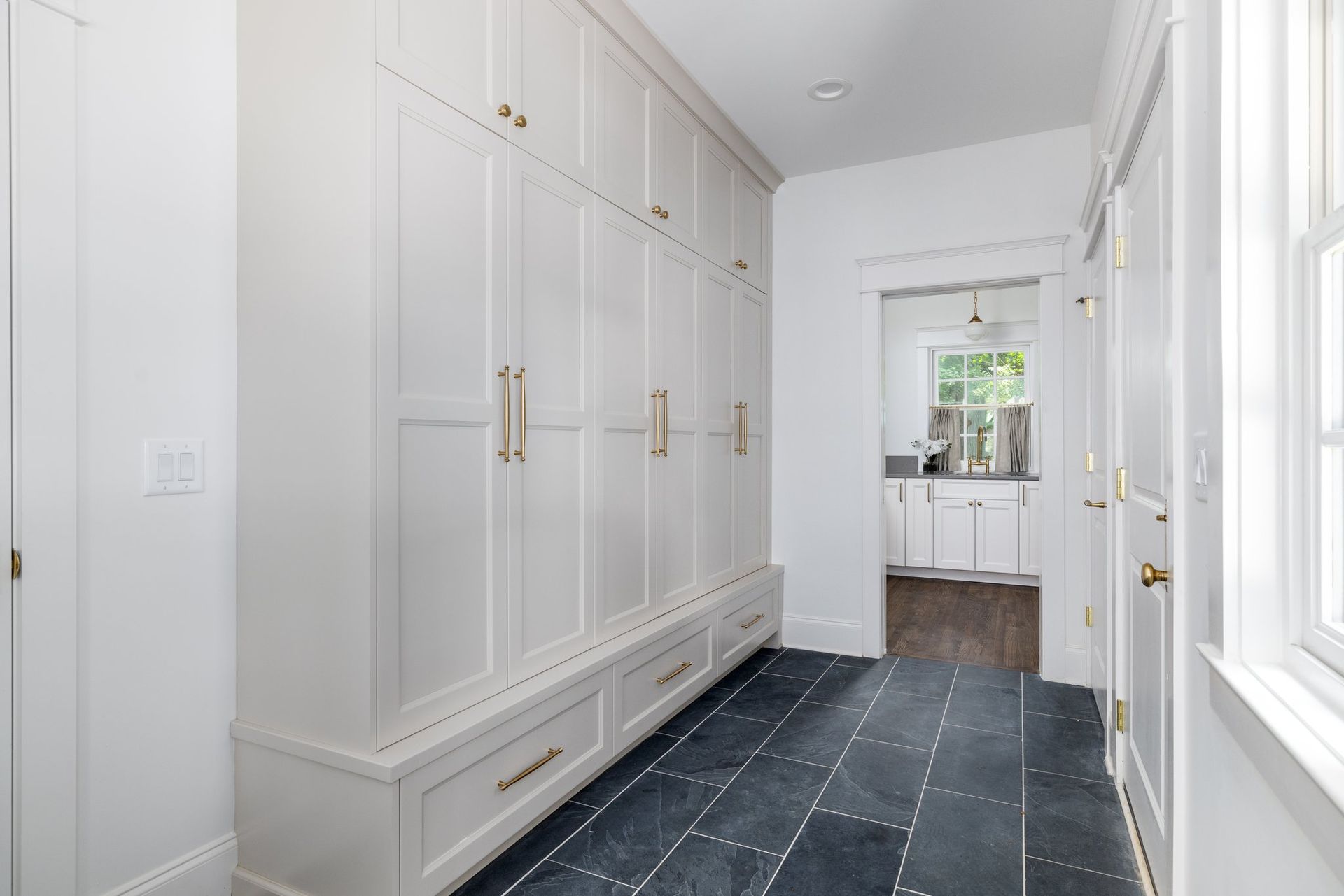 White hallway with built-in cabinets, dark slate tile floor, door to kitchen visible at the end.