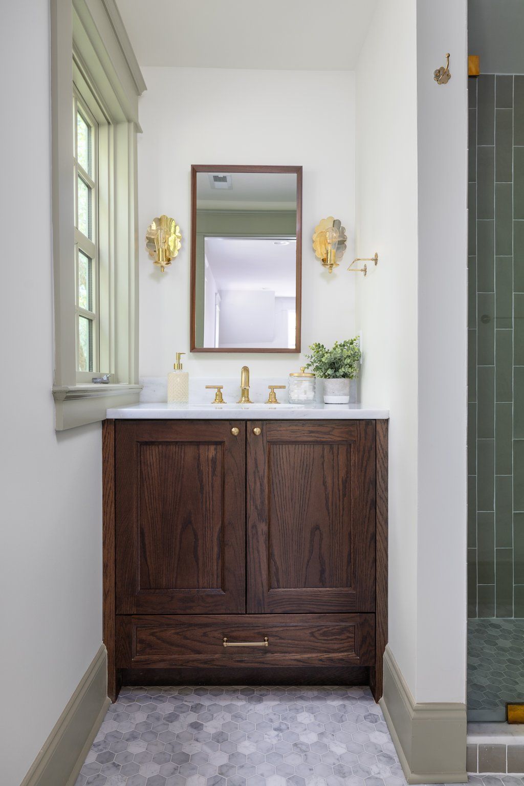 Dark wood vanity in a bathroom with gold accents, white walls, and a small window.