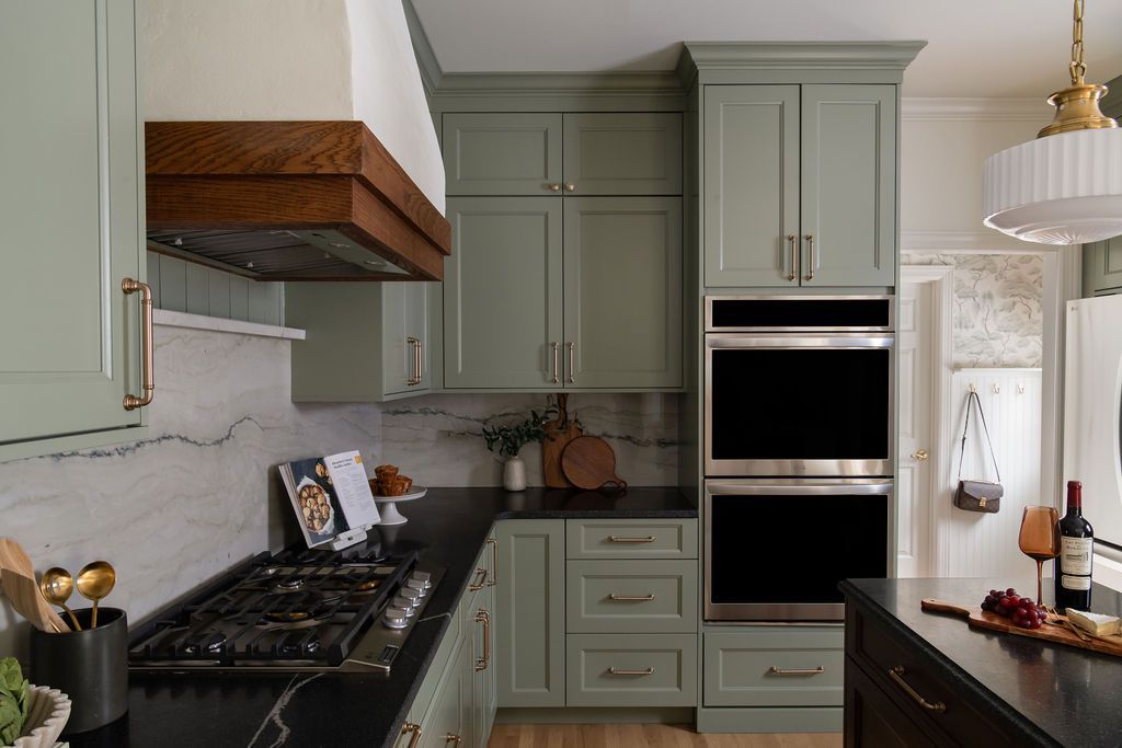 Green kitchen with dark countertops, wood range hood, and double oven.