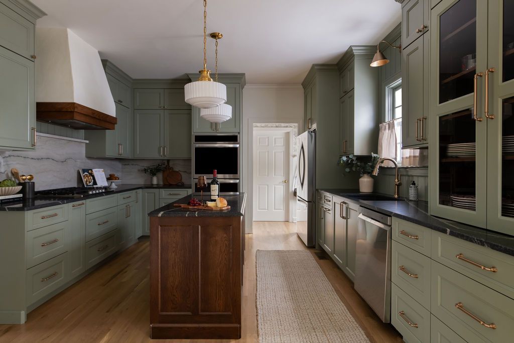 Sage green kitchen with dark wood island, stainless steel appliances, and white accents.