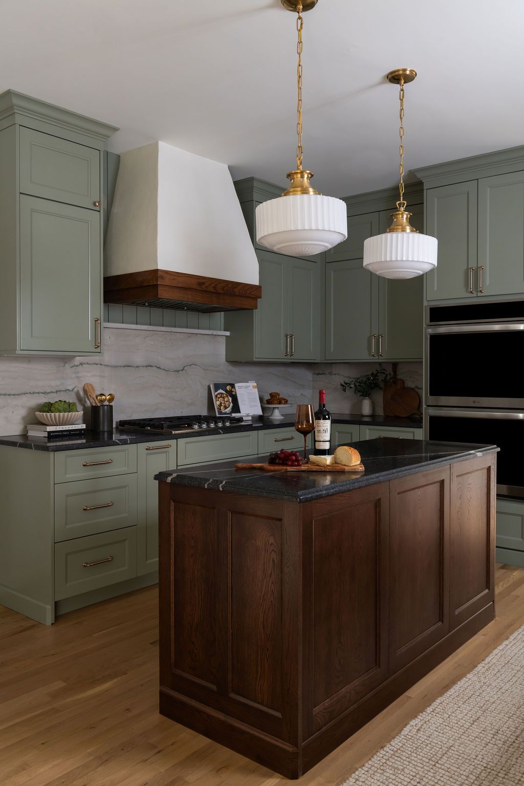 Sage green kitchen with dark wood island, white range hood, and gold pendant lights.
