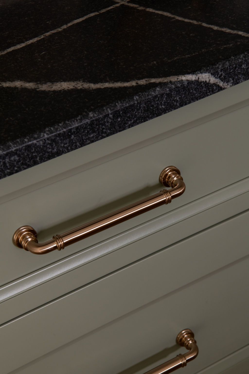 Olive green kitchen cabinets with copper pipe-style handles beneath a dark granite countertop.