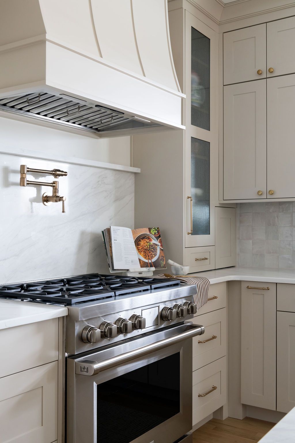 Stainless steel range with a white range hood in a light-colored kitchen with built-in cabinetry.