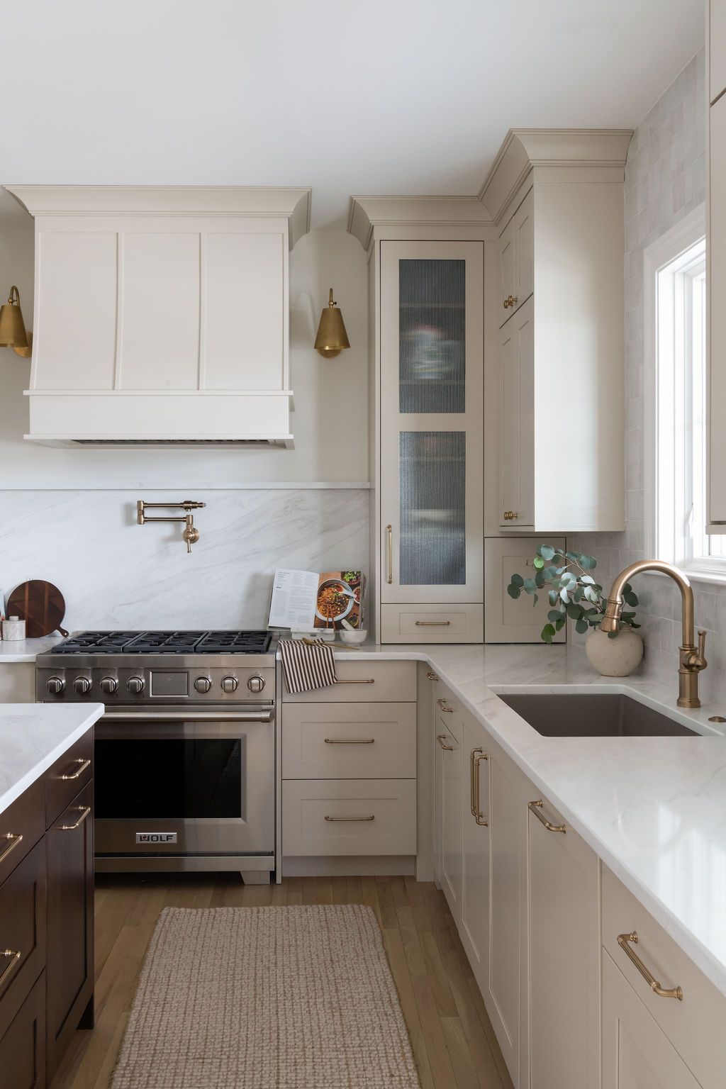 Beige and white kitchen with stainless steel appliances, marble backsplash, and wooden flooring.