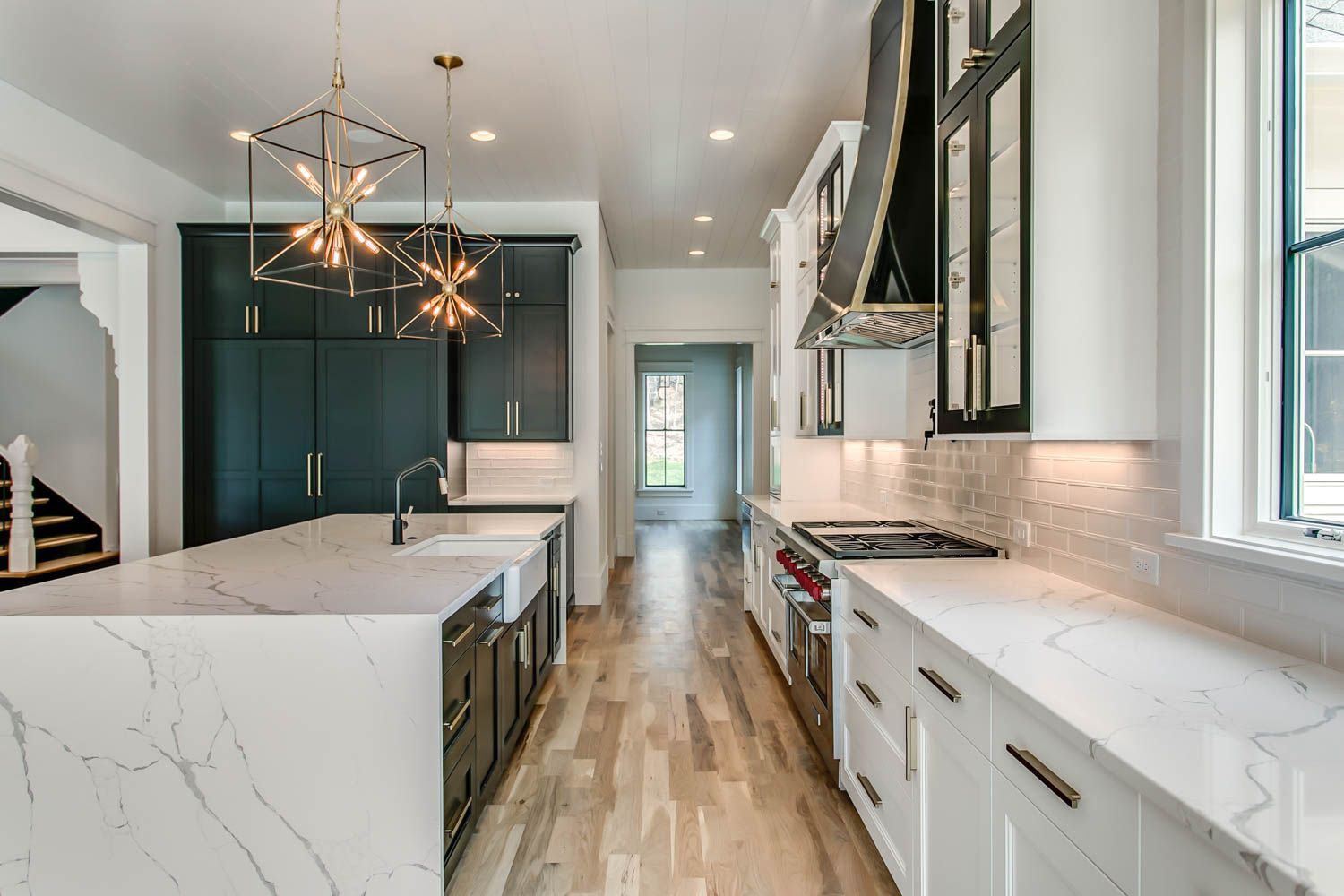 Modern kitchen with white countertops, dark cabinets, gold light fixtures, and wooden floors.
