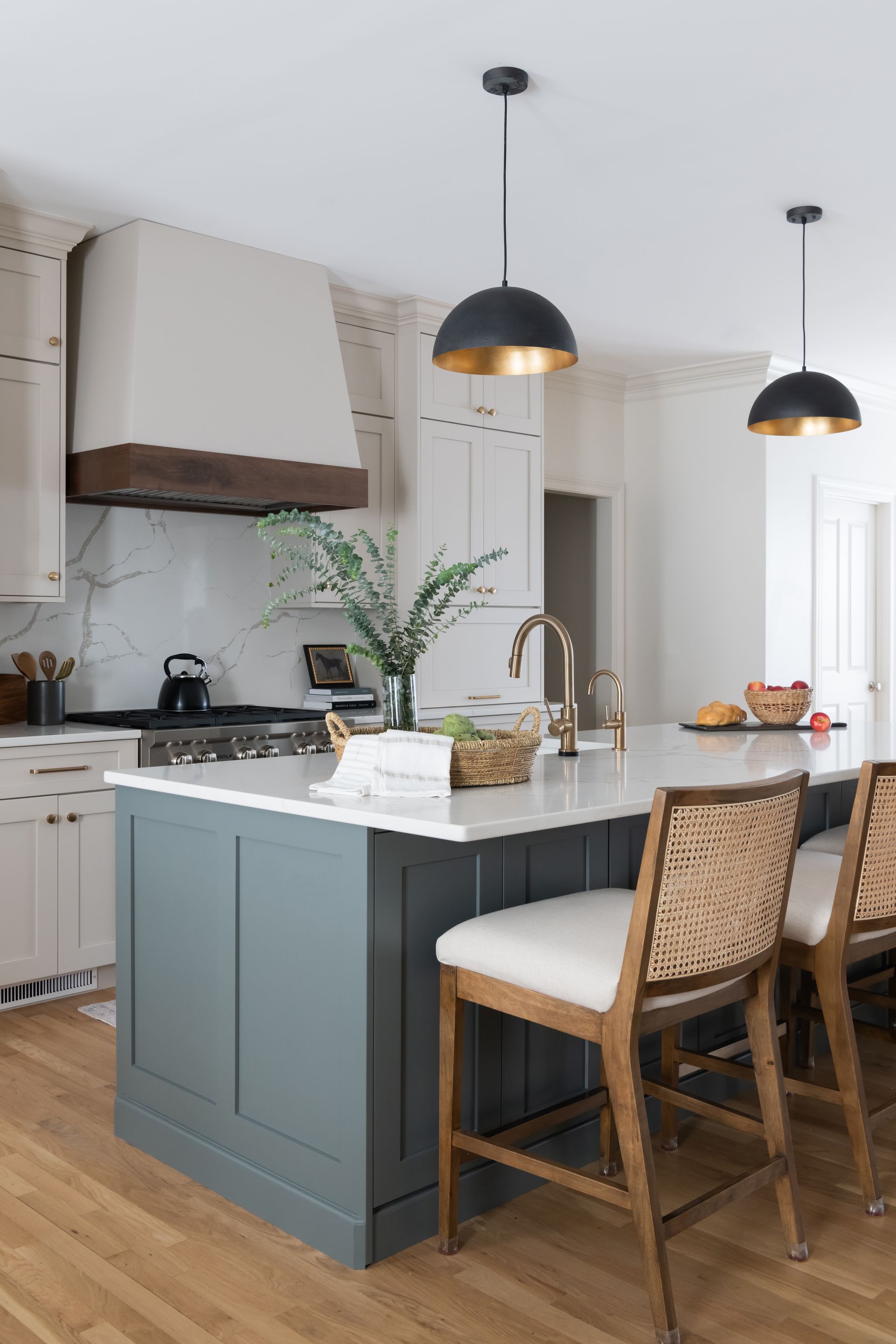 Kitchen with blue island, white countertops, and black pendant lights. Woven barstools sit at the island.