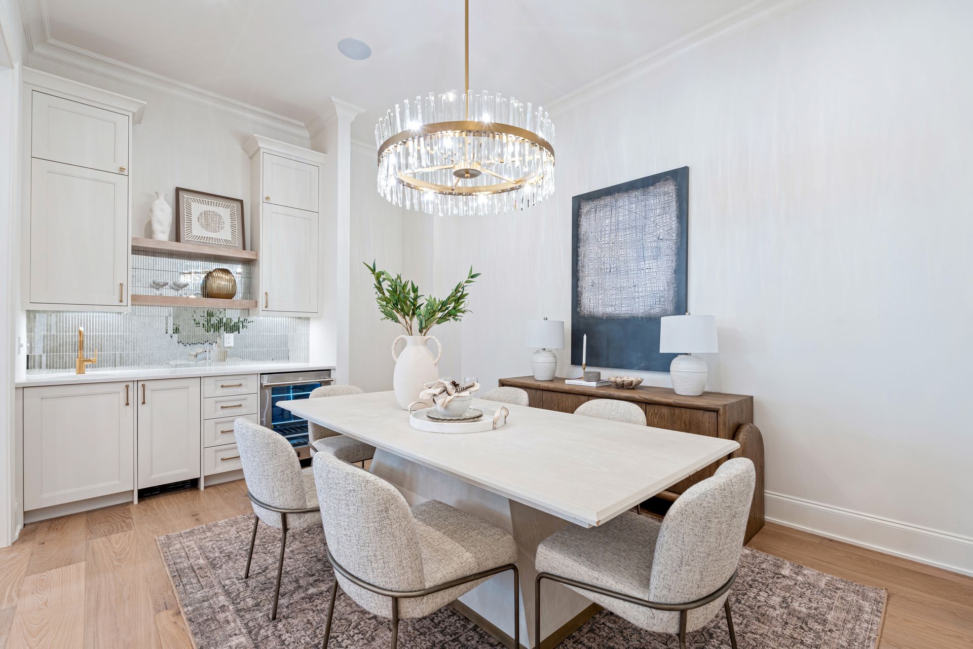 Elegant white dining room with marble table, crystal chandelier, and sideboard.