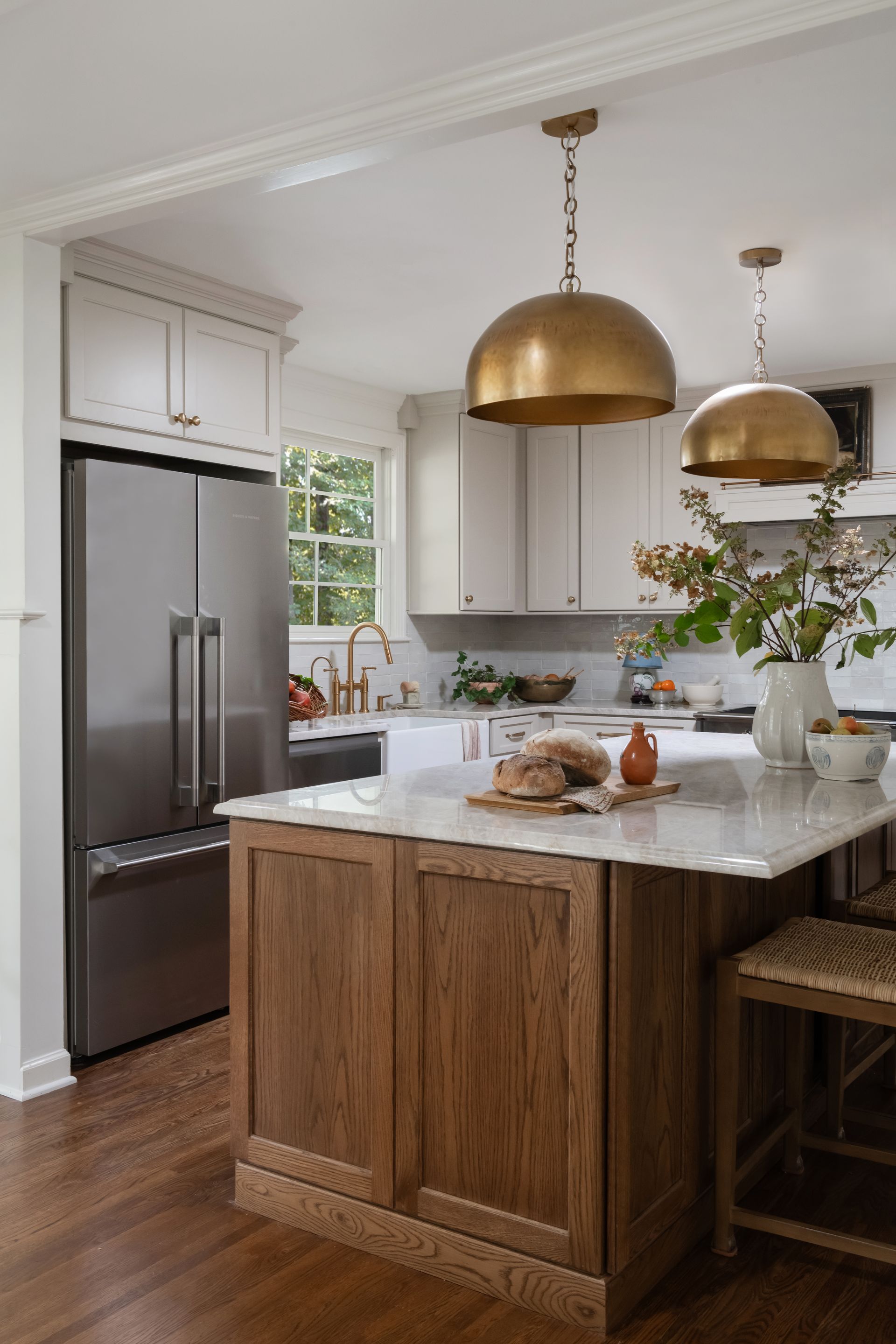 Kitchen with gold pendant lights, island with wooden cabinets and white countertop, stainless steel refrigerator.