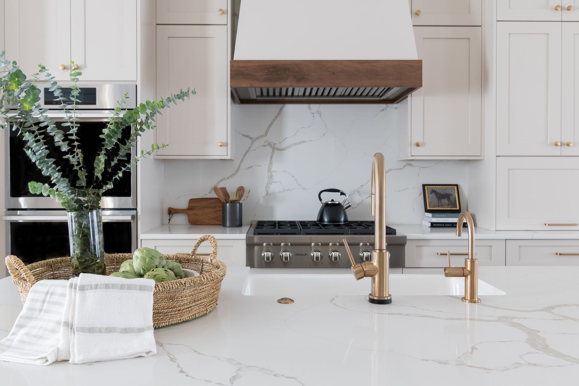 Kitchen with white cabinets, gold fixtures, marble countertop, and wood range hood.
