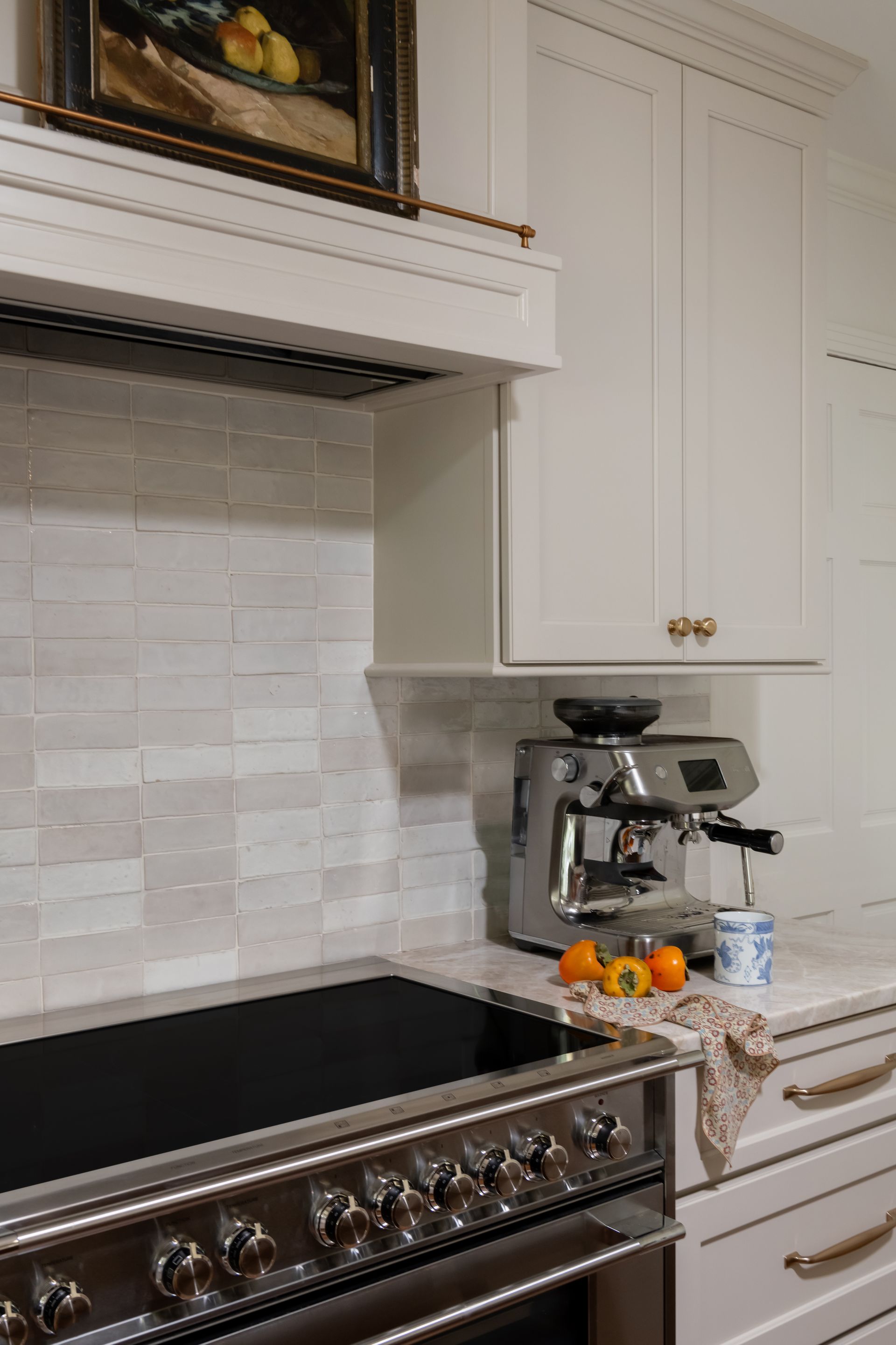 Kitchen with white cabinets, light tile backsplash, range, and espresso machine on counter.