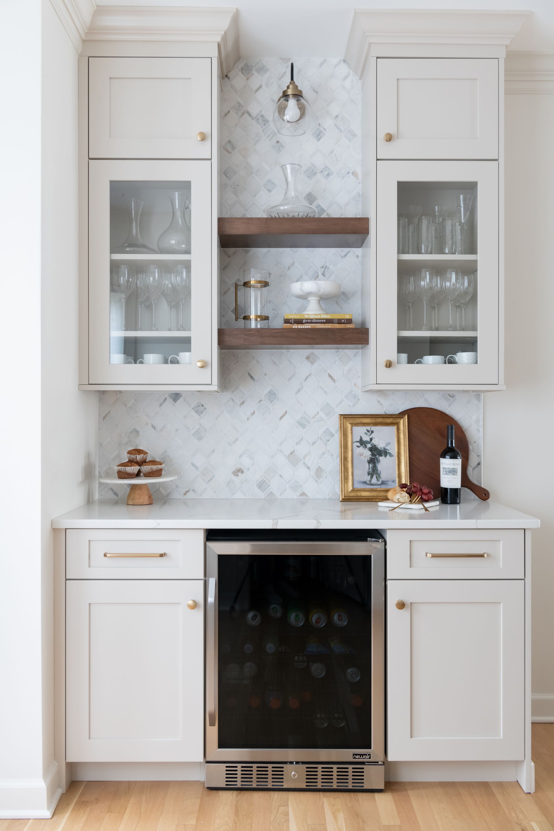 A home bar area with cream cabinets, wine fridge, and decorative shelving against a patterned backsplash.