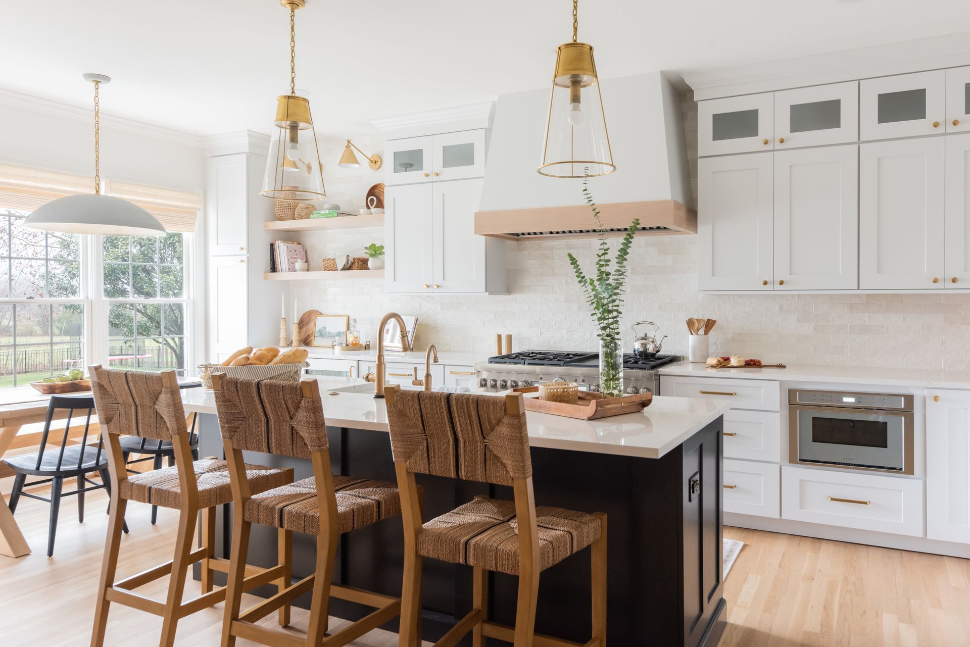 Modern kitchen with white cabinets, dark island, gold accents, and woven bar stools.