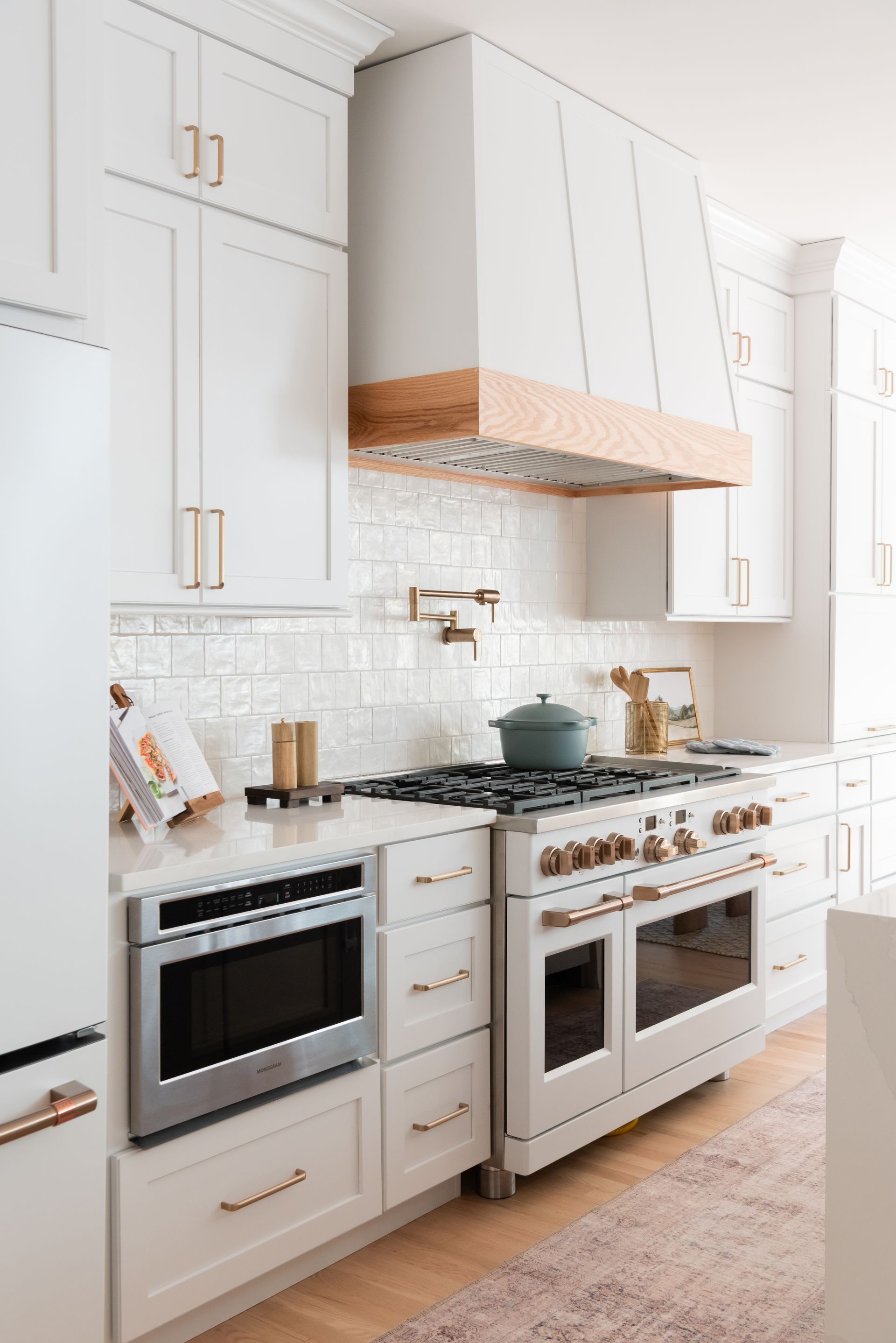 White kitchen with oven, range hood, and cabinets. Light wood accents and stainless steel appliances.